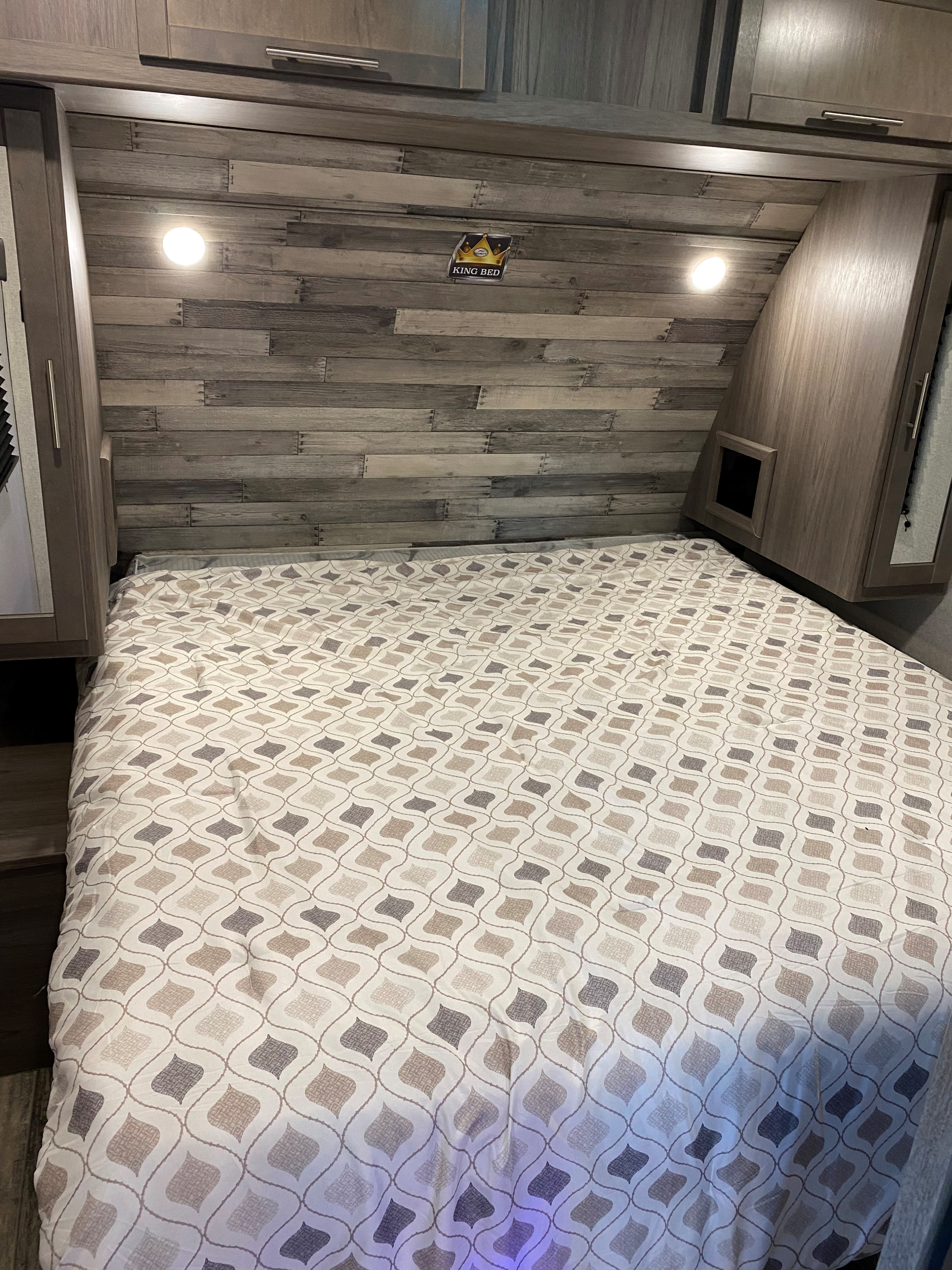 An inviting RV rental bedroom with a king bed, patterned comforter, wood-paneled headboard, and overhead storage.. Crossroads RV Volante 2021
