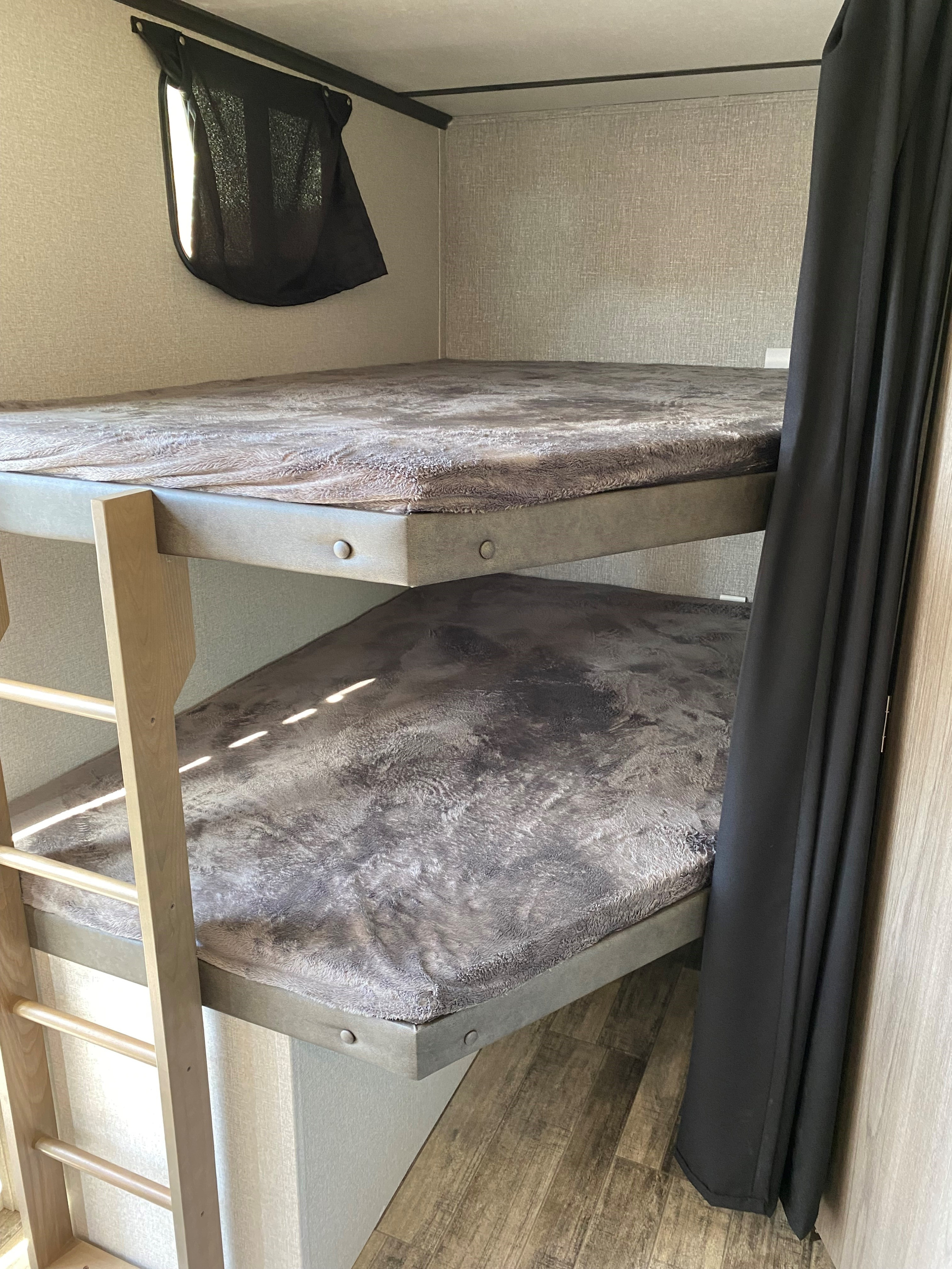 Inside an RV rental, two bunk beds with soft grey bedding, a wood ladder, and black privacy curtains create a cozy sleeping area.. Crossroads RV Volante 2021