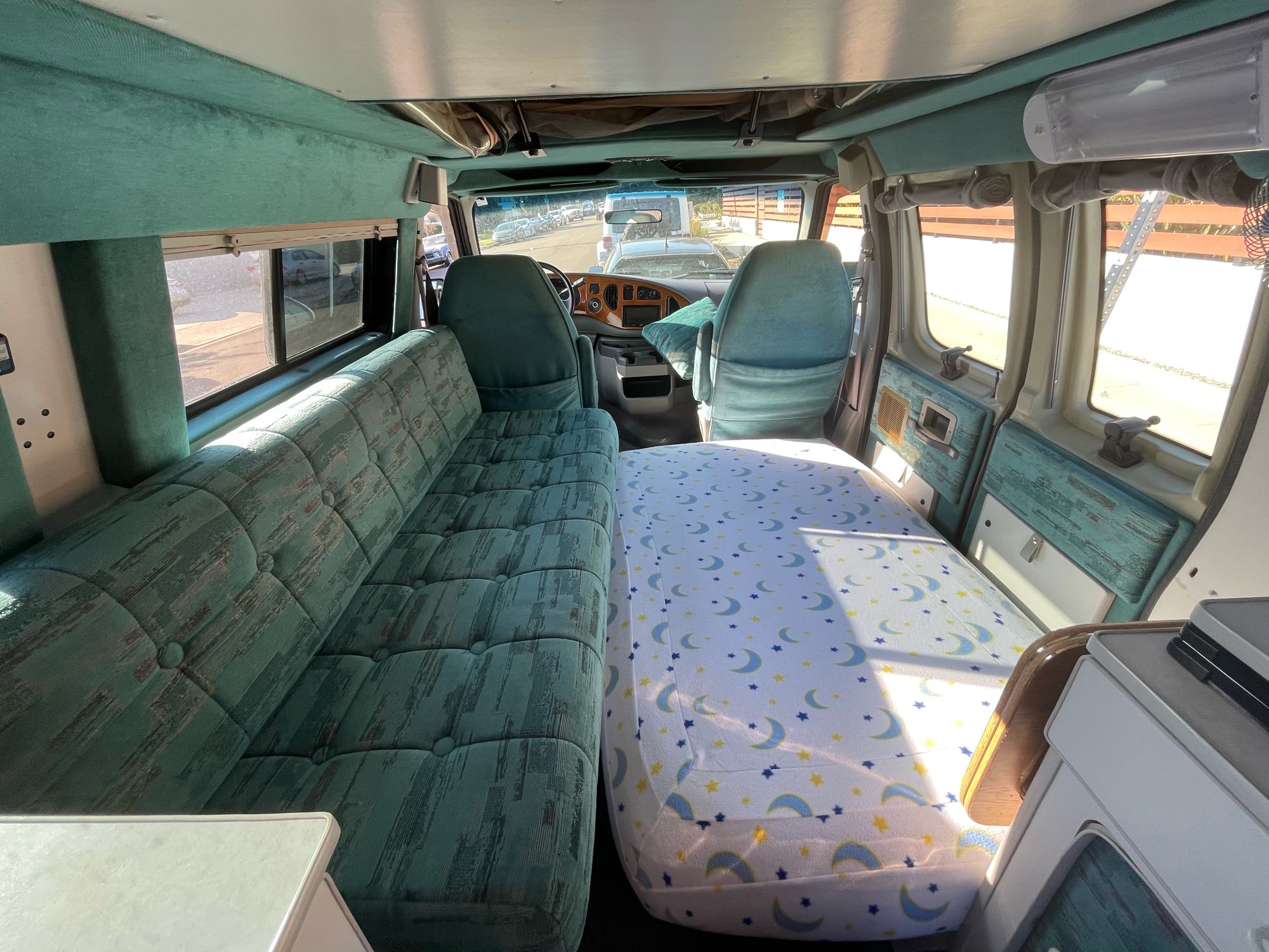 RV rental interior: cozy green sofa, moon/star bed, and driver's cabin. Perfect camper van for your next adventure.. Sportsmobile E350 1997