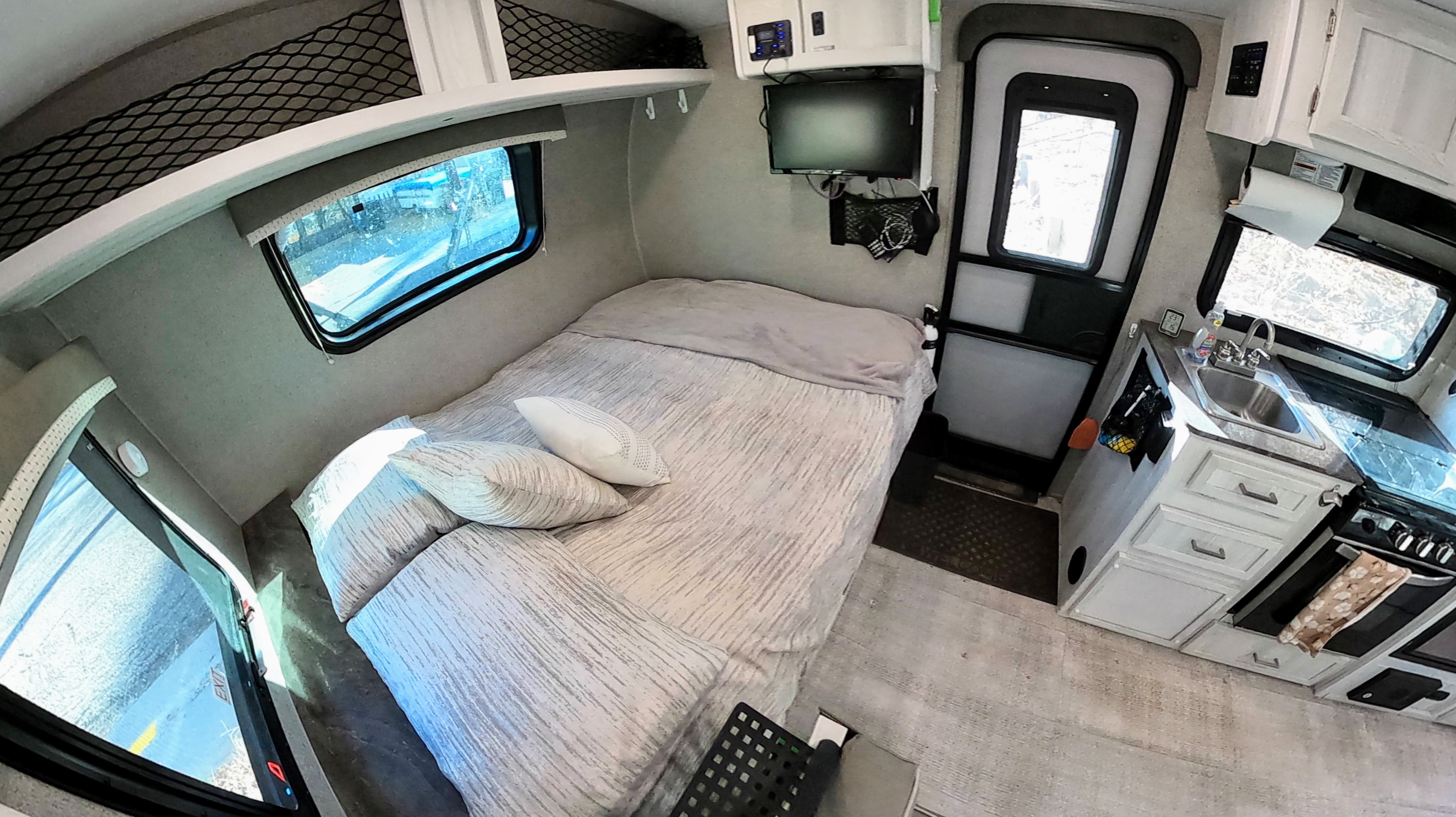 Inside an RV rental: cozy bedroom area with a striped comforter and pillows, integrated kitchenette, and TV for compact living.. Forest River Rockwood 2021