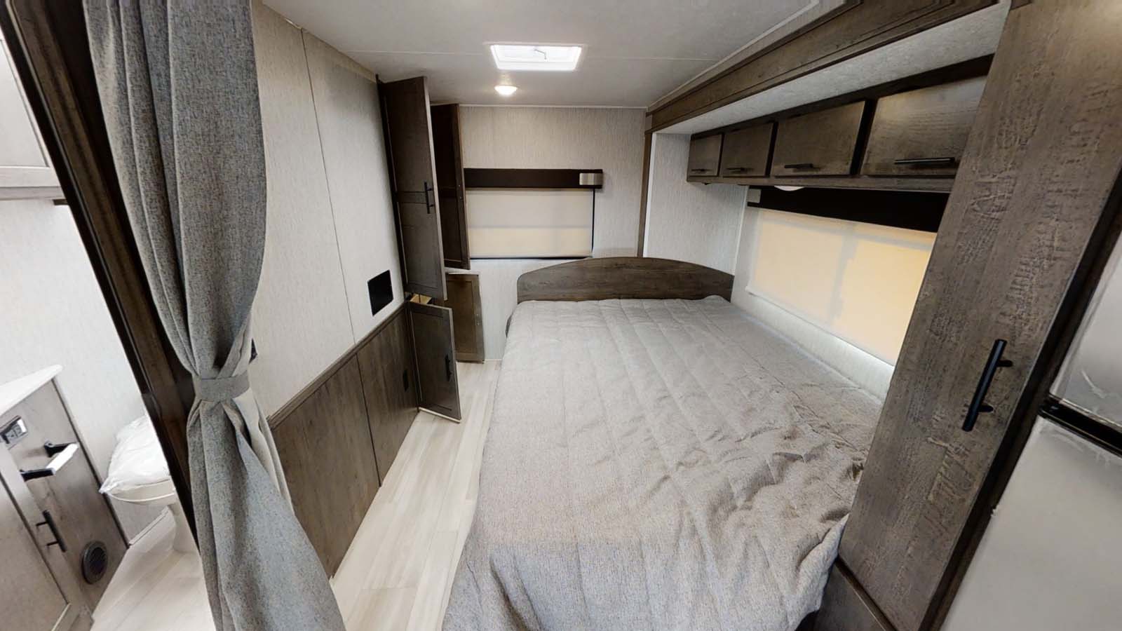 RV rental bedroom with a comfortable bed, dark wood cabinets for storage, and a bright window. Ideal for compact living.. Forest River Coachmen Leprechaun 2021