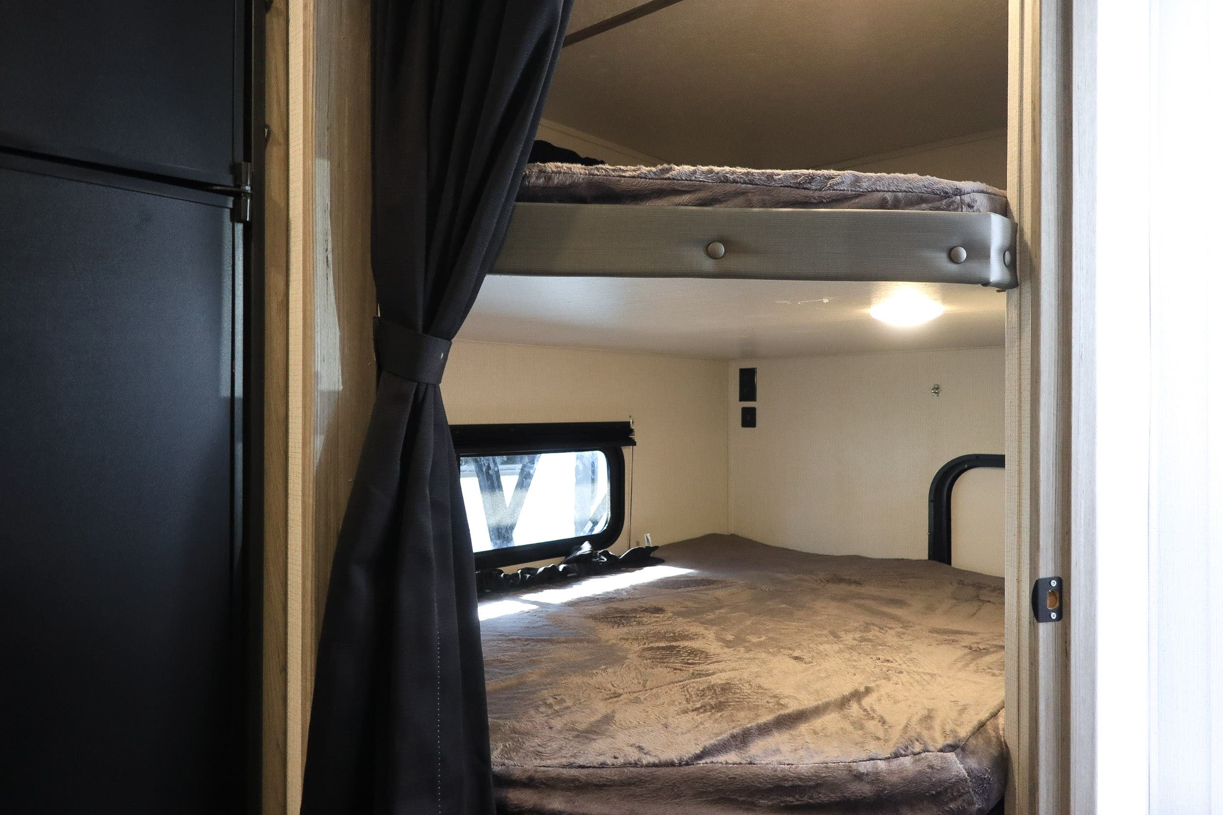 RV rental's bunk beds, showcasing a cozy sleeping area with a window, a light, and a black refrigerator.. KeyStone Passport SL 221BH 2022