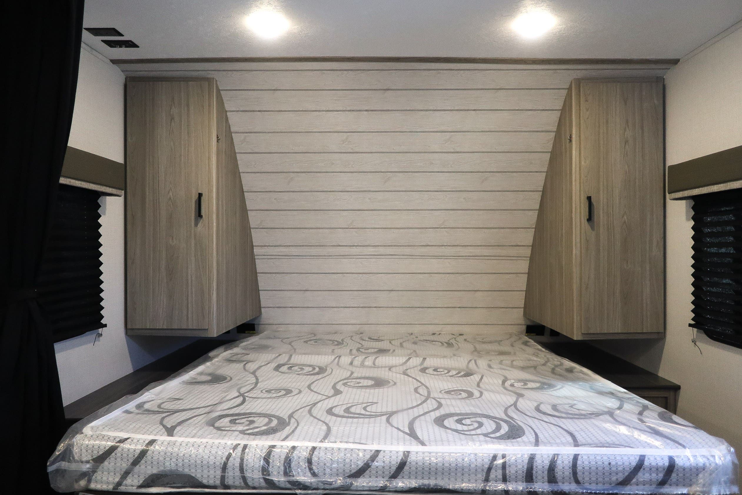 RV rental bedroom: Mattress with protective plastic, sleek wood-paneled wall, and practical overhead storage.. KeyStone Passport SL 221BH 2022