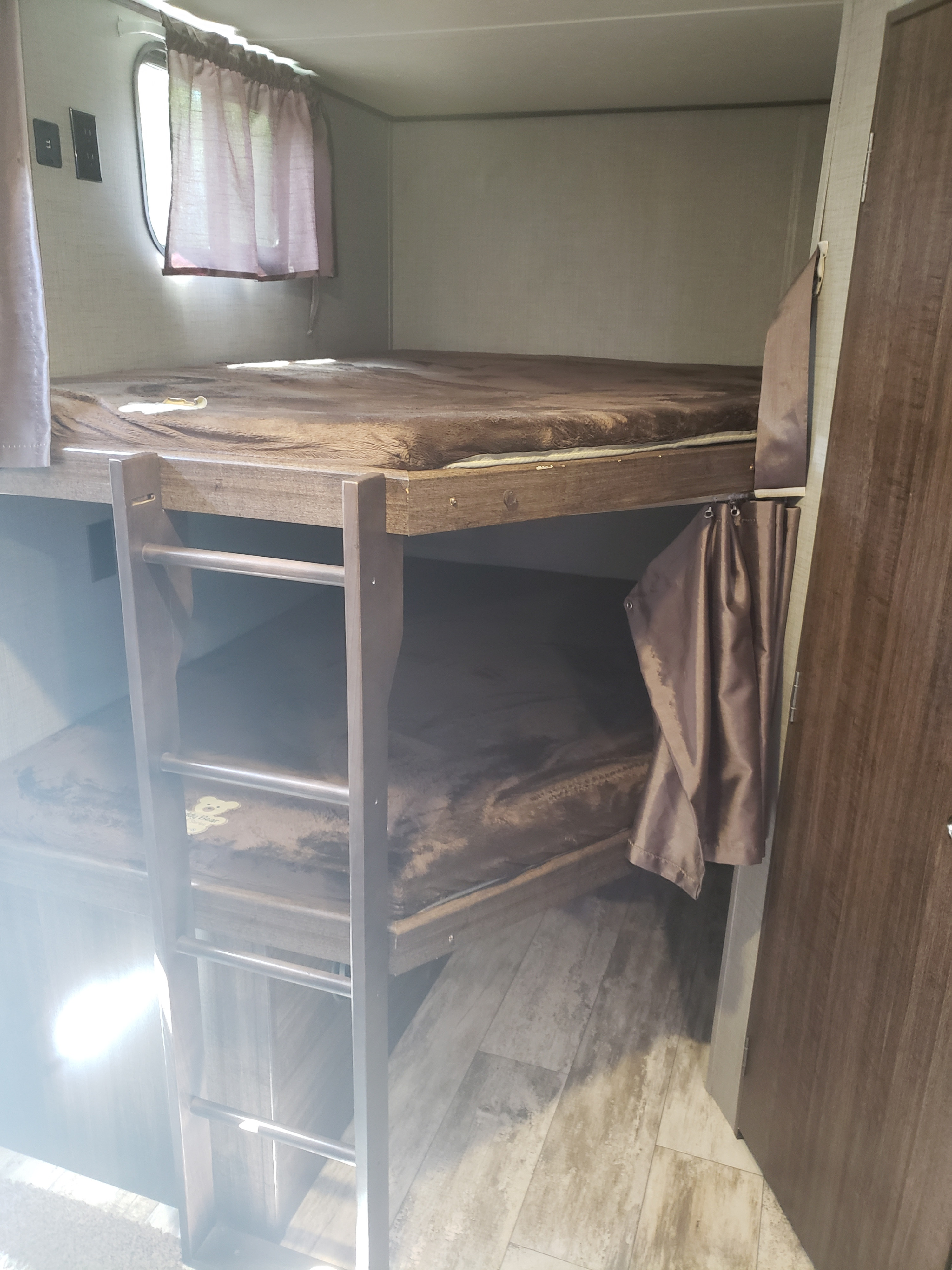 Cozy bunk beds in an RV rental interior, featuring a ladder, window with curtains, and plush bedding, ideal for family trips.. Crossroads RV Zinger 2018