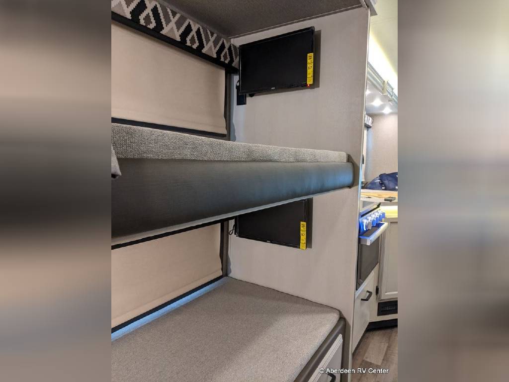 This rv rental features two stacked bunk beds, each with a personal TV. A compact RV interior with a partial view of the kitchen.. Jayco Greyhawk 2022