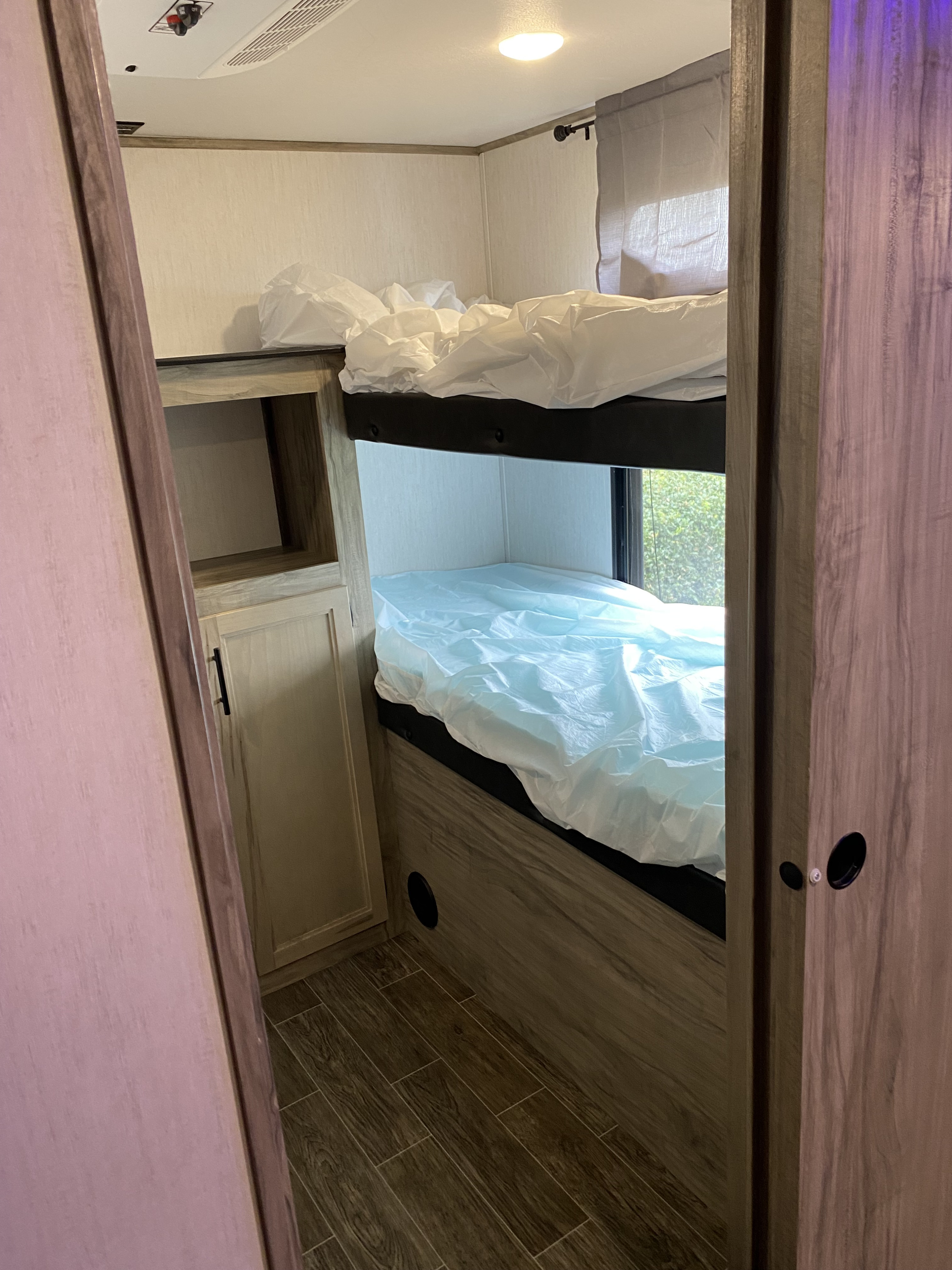 Clean RV rental bunk beds with protective covers, built-in storage, and window view, ready for your adventure.. Forest River Cherokee Alpha Wolf 2021