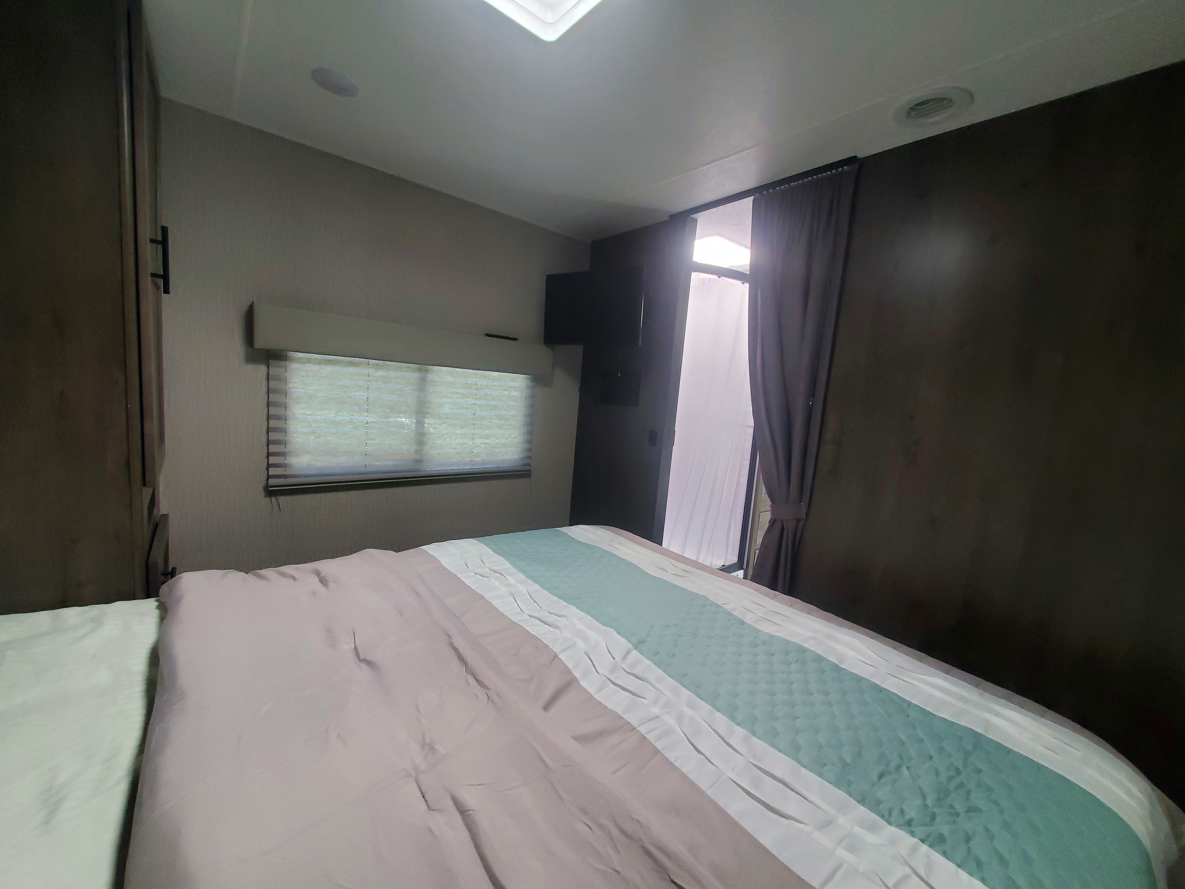 Inside a comfortable RV rental bedroom featuring a striped comforter, window blinds, and side exit with curtains.. Other Other 2022