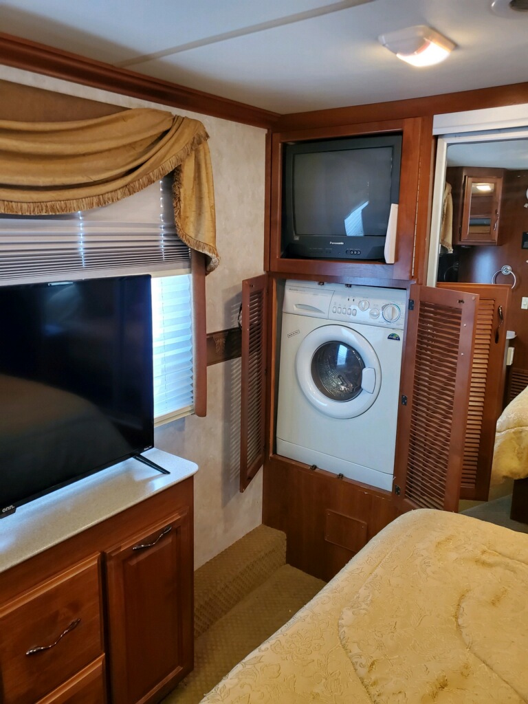RV rental interior showing bedroom area, modern TV, and built-in compact washer/dryer under a CRT TV in a motorhome.. Fleetwood Discovery 2004