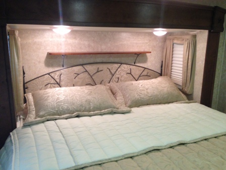 Cozy RV bedroom in an RV rental, featuring a comfy bed, unique headboard, and overhead lights for your next travel adventure.. Open Range Open Range BH2 2013