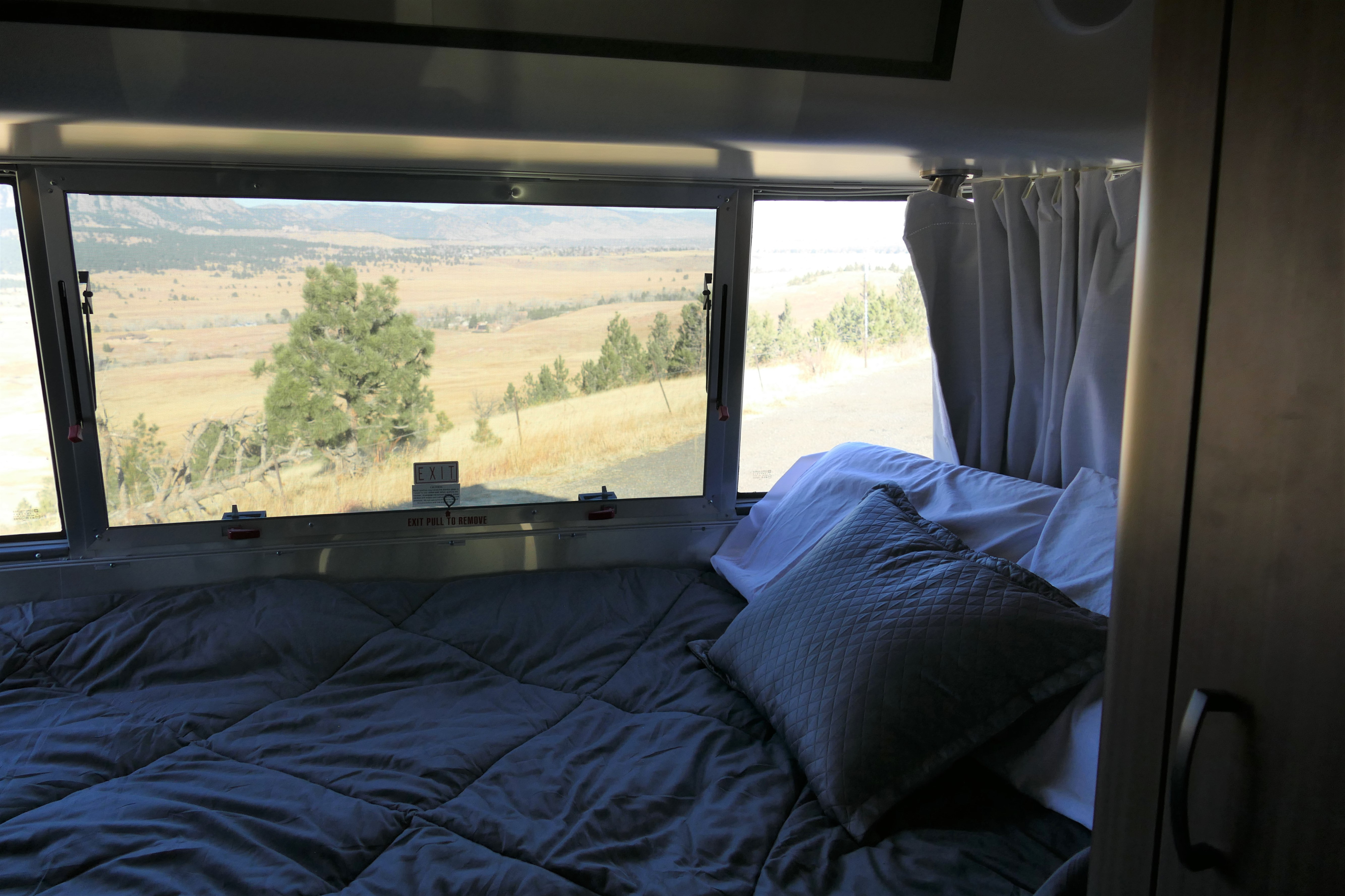 Cozy RV rental bedroom offering a stunning landscape view through the window. Experience comfort and nature on your travels.. Airstream Caravel 2020