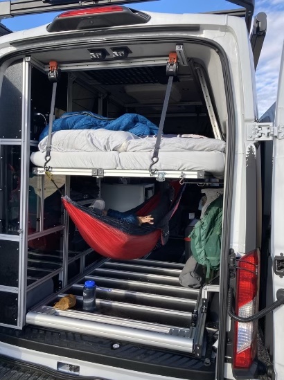 Customized RV rental interior features a suspended bed above a red hammock with a person relaxing, optimizing space.. Ford Transit 2019