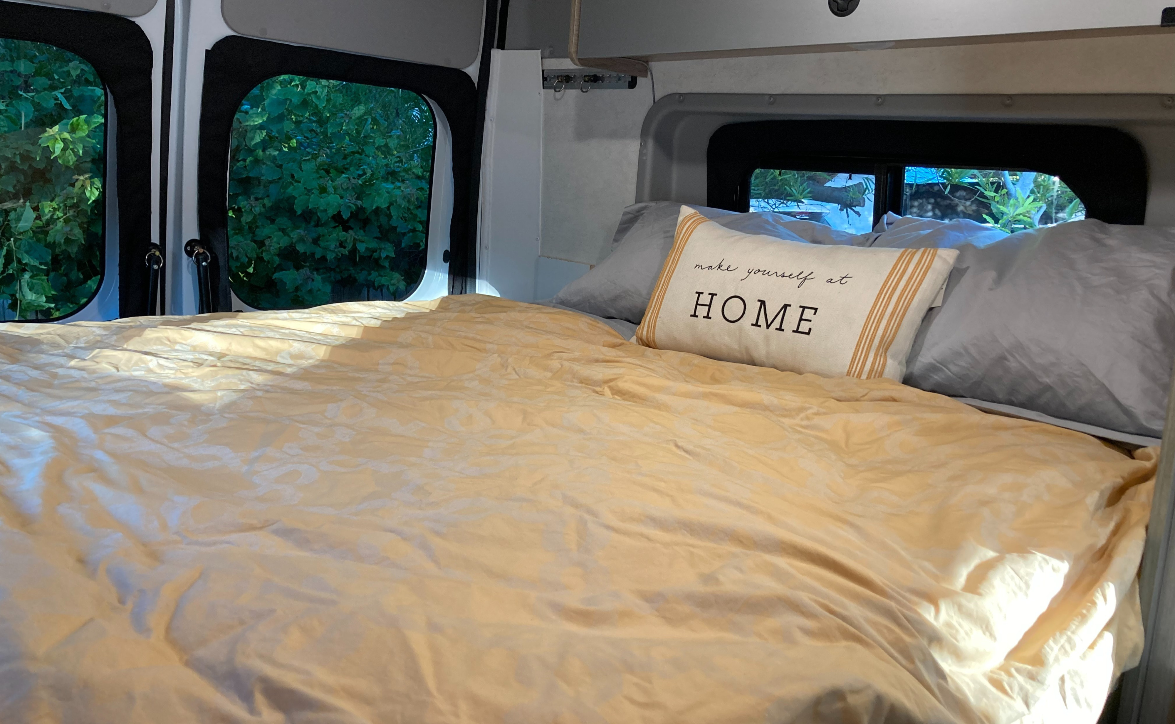 Cozy RV rental bed with "make yourself at HOME" pillow and nature views outside, creating a comfortable travel space.. Winnebago Solis 59PX 2022