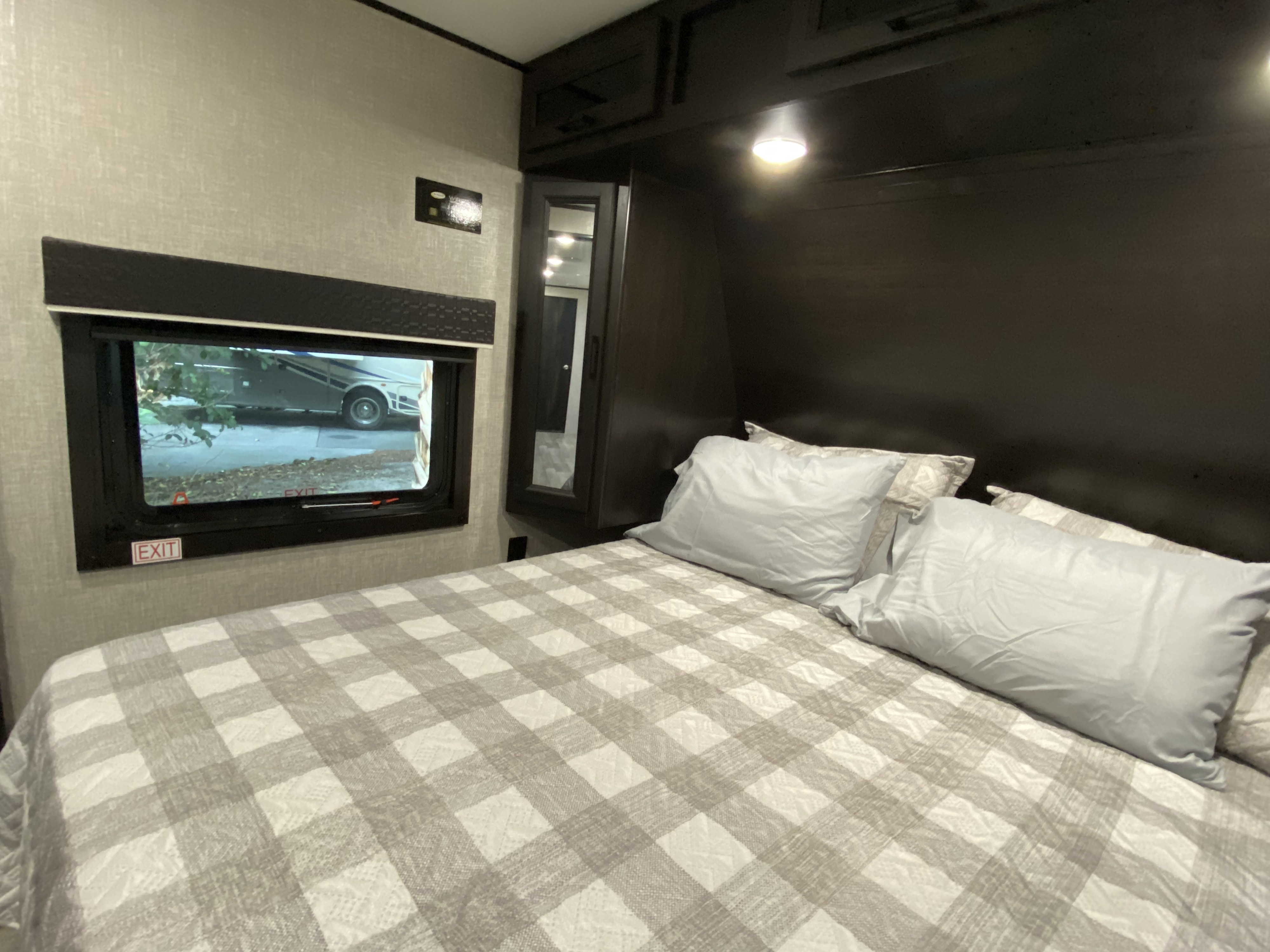 Inside a spacious RV rental bedroom: cozy plaid bed, window with exit sign, and wall controls for your comfortable journey.. Jayco Jay Flight 2022