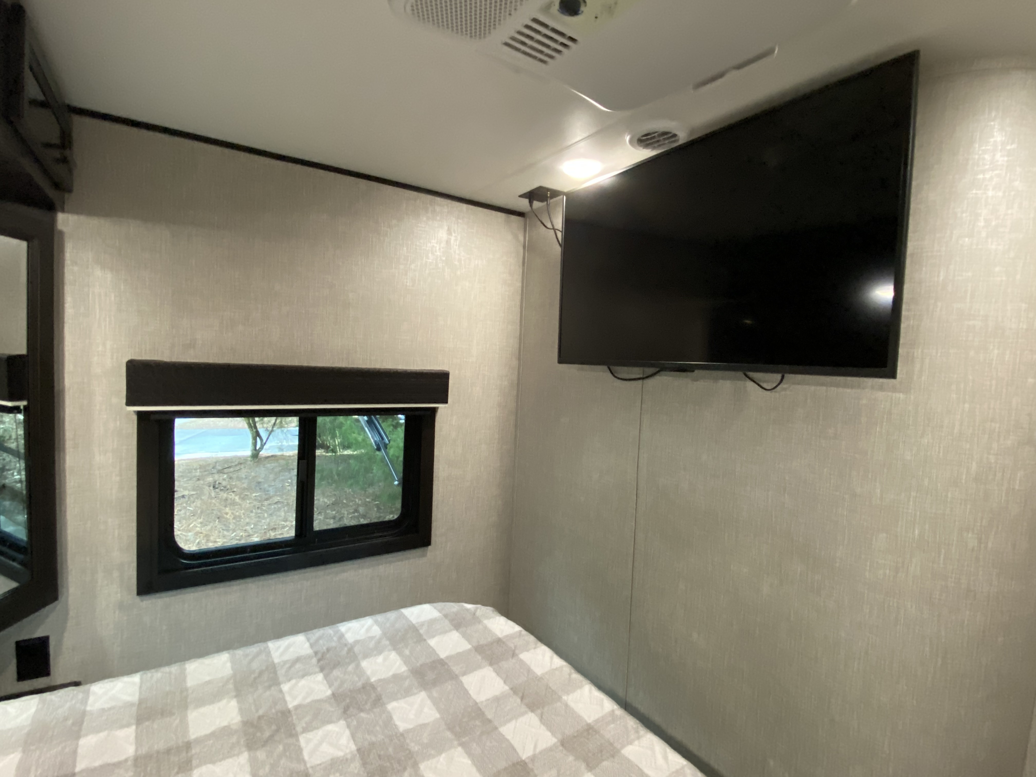 Cozy rv rental bedroom with a plaid bed, a window looking outside, and a wall-mounted TV.. Jayco Jay Flight 2022