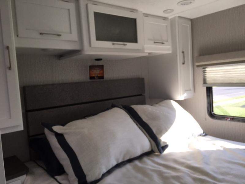 Experience comfort in this RV rental bedroom: a cozy bed, white overhead cabinets, and a window bringing in light.. Forest River Coachmen Pursuit 2022