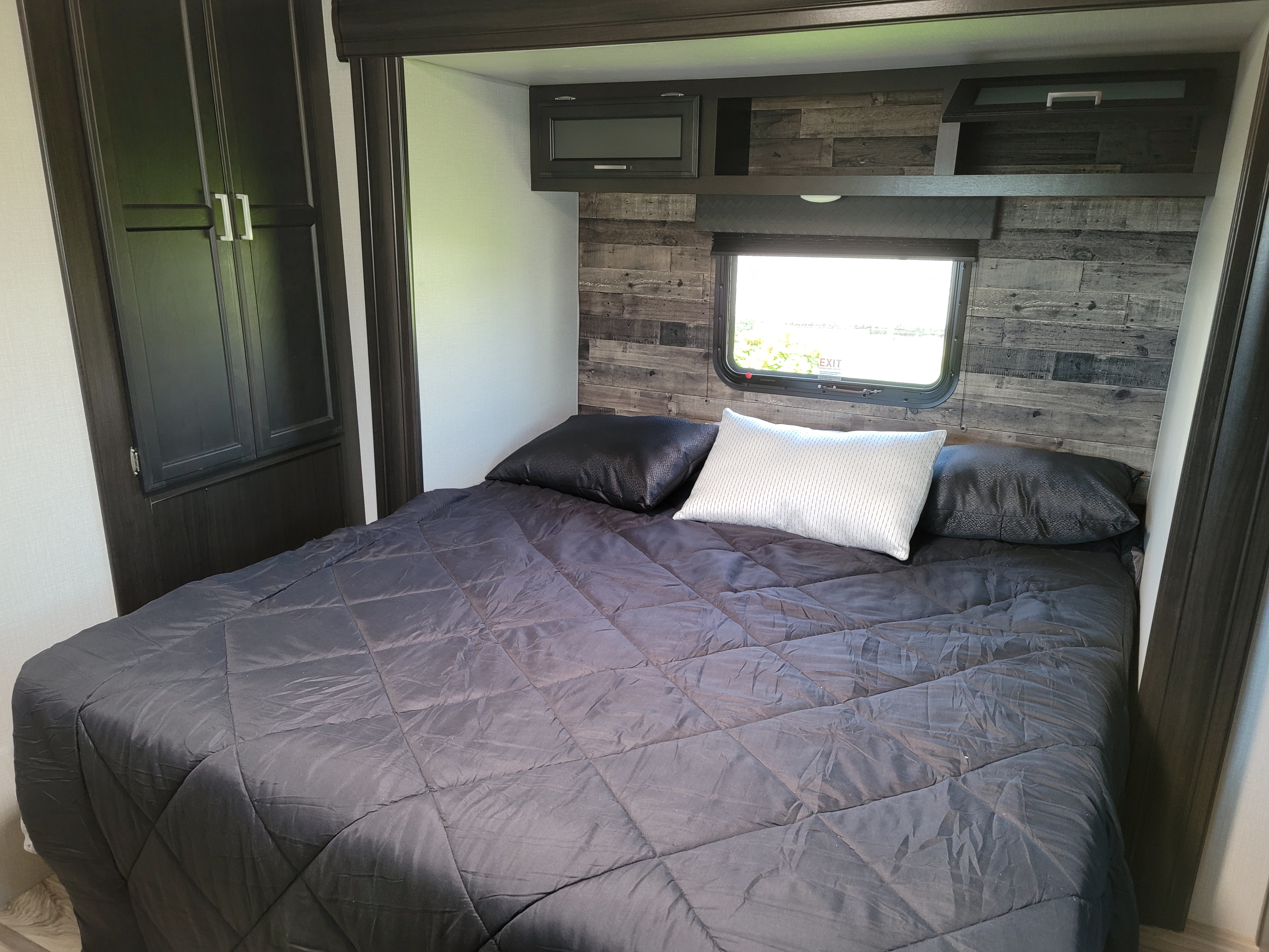 Cozy RV rental bedroom featuring dark bedding, wood-plank walls, and built-in storage.. Venture Rv Sporttrek 2021