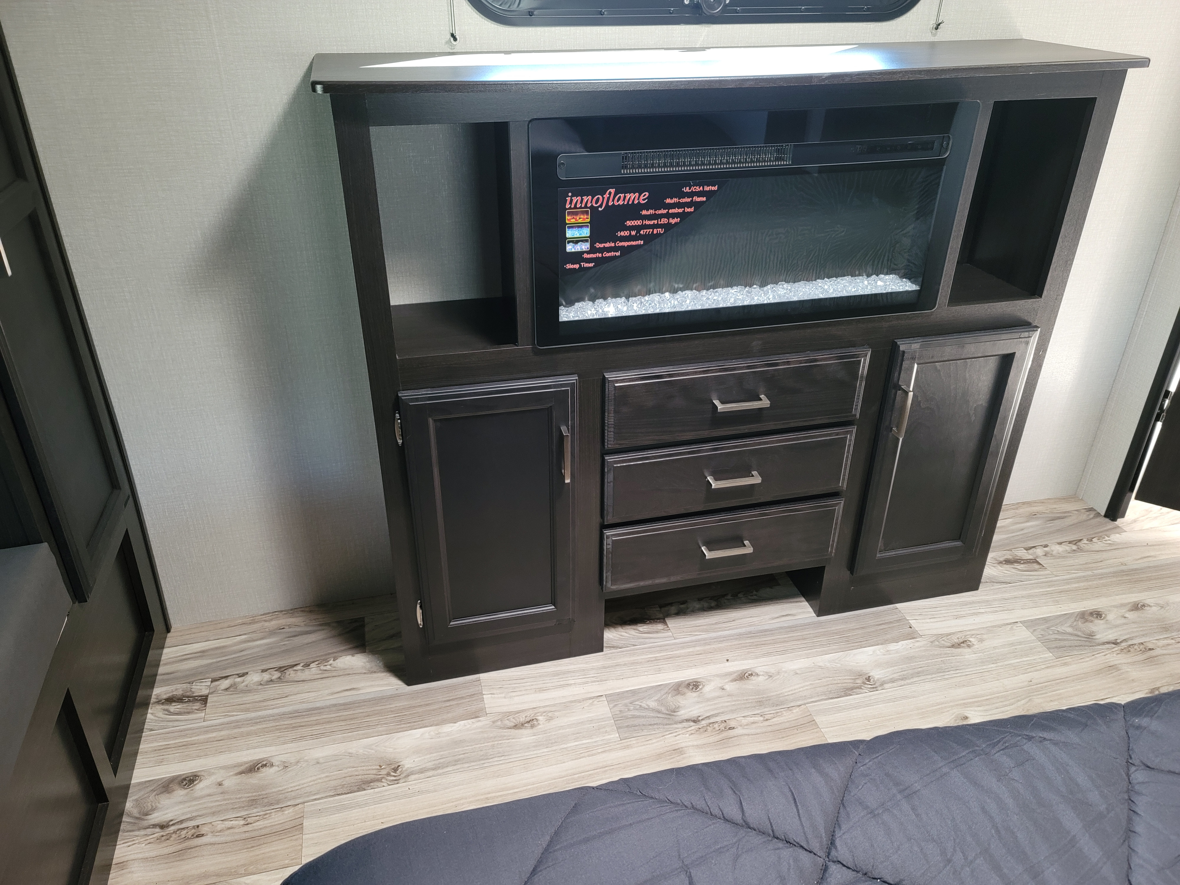 Modern RV rental: Dark wood cabinet featuring an innoflame electric fireplace, storage shelves, and drawers, enhancing the living space.. Venture Rv Sporttrek 2021