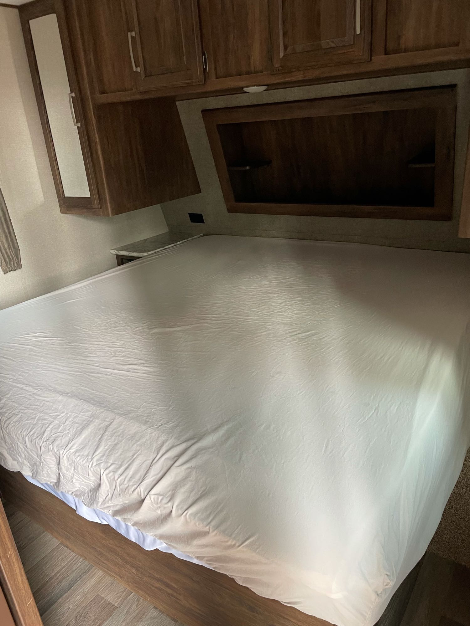 Interior of an RV rental bedroom showing a large bed with a light sheet, wooden cabinets, and ample storage.. Keystone Cougar Half-Ton 2017