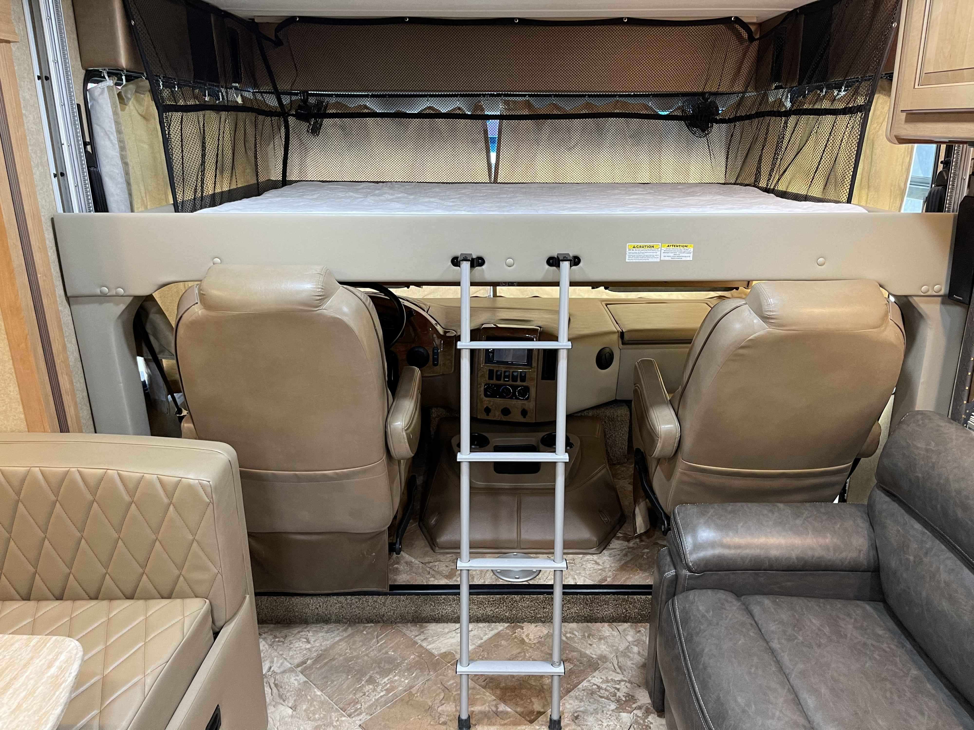 Inside an RV rental: a large overhead bunk bed with ladder, safety net, and the front driver's area below.. Other Other 2016