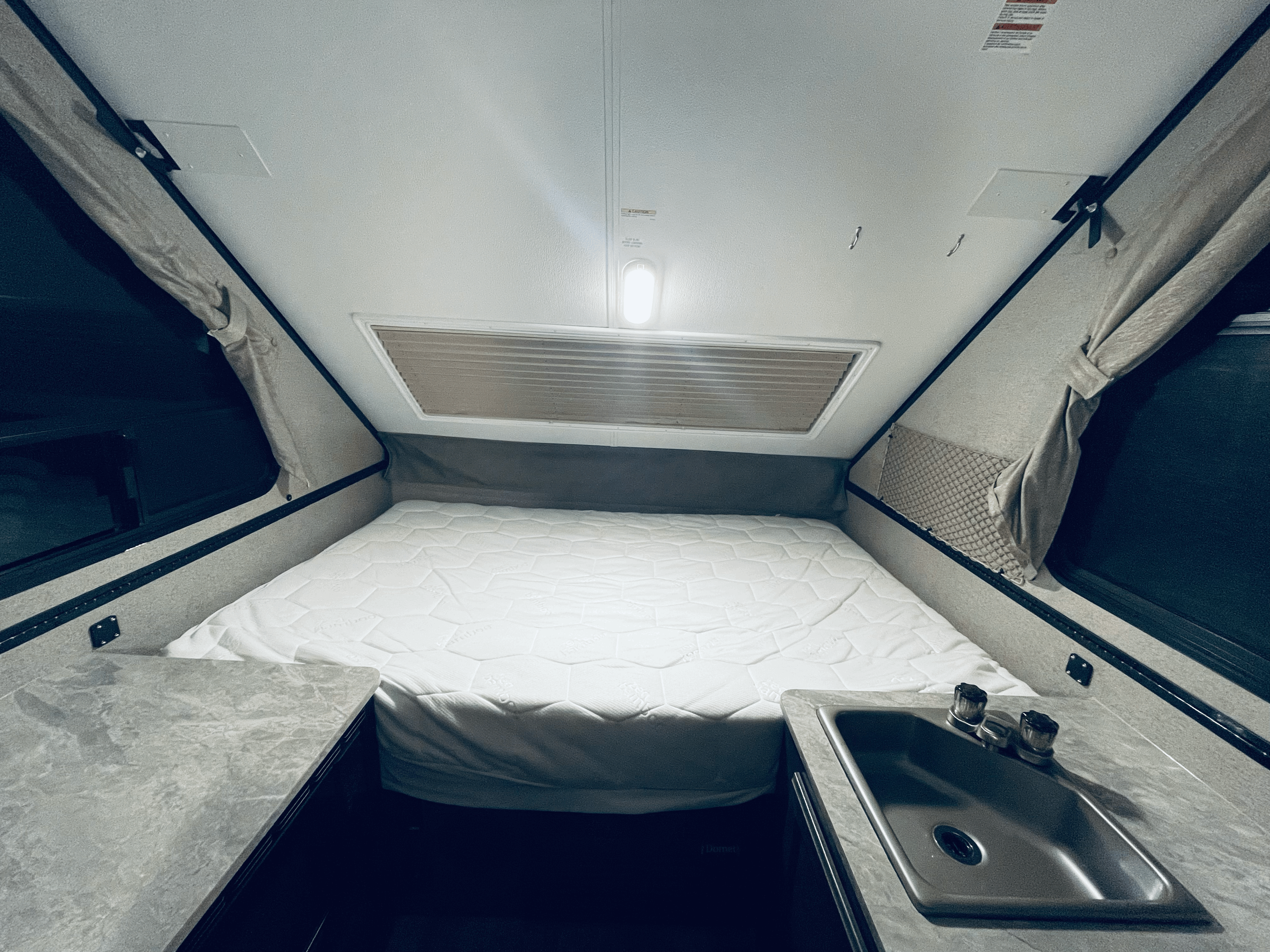 Interior of an rv rental with a large bed, sink, and pop-up walls, ready for your next adventure.. Forest River Rockwood Premier 2020