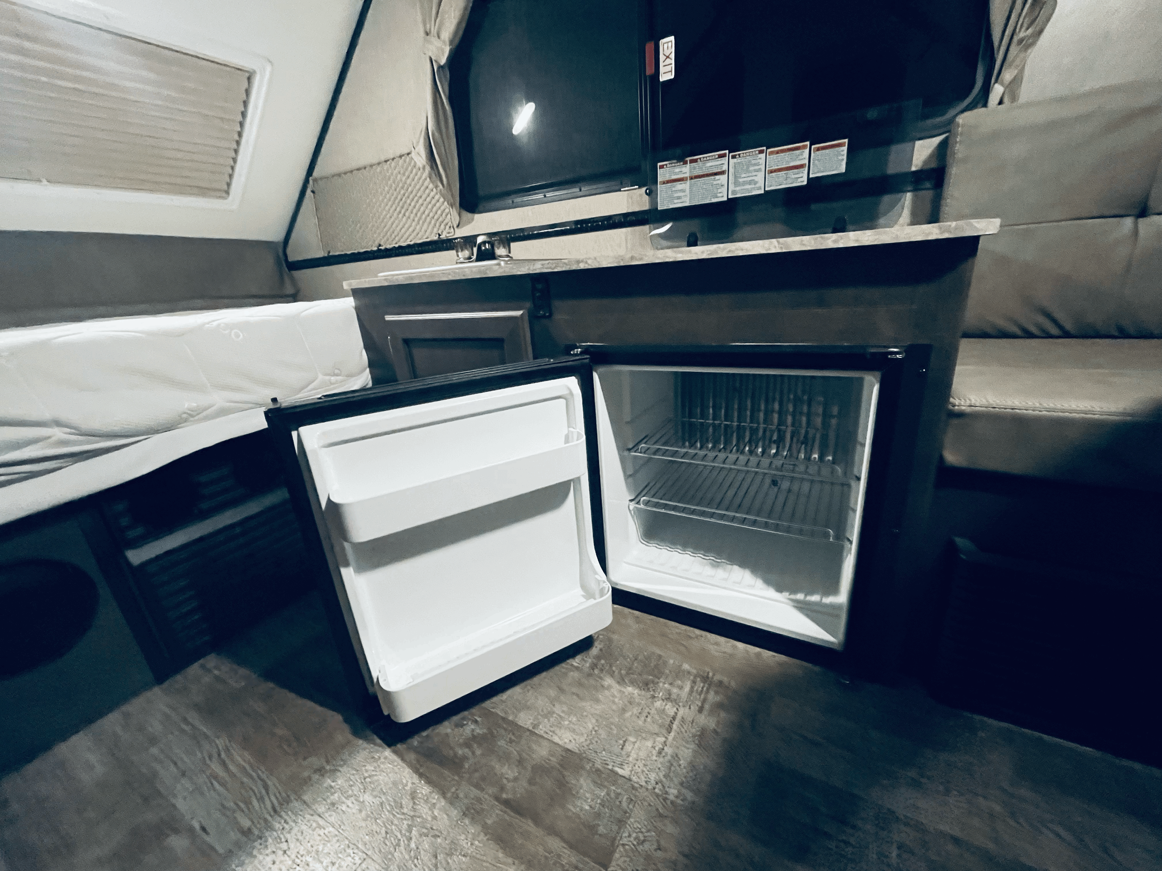 This RV rental interior offers a compact space with an open mini-fridge, a bed, and a mounted TV above a counter.. Forest River Rockwood Premier 2020