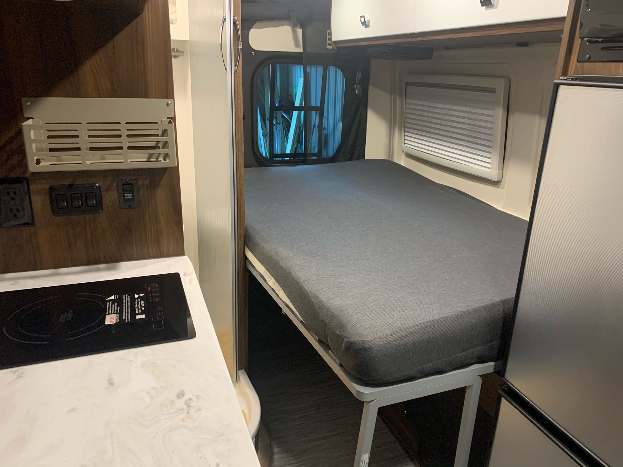 RV rental interior: cozy bed, compact kitchen with induction cooktop, and smart storage for road adventures.. Winnebago Travato 2022