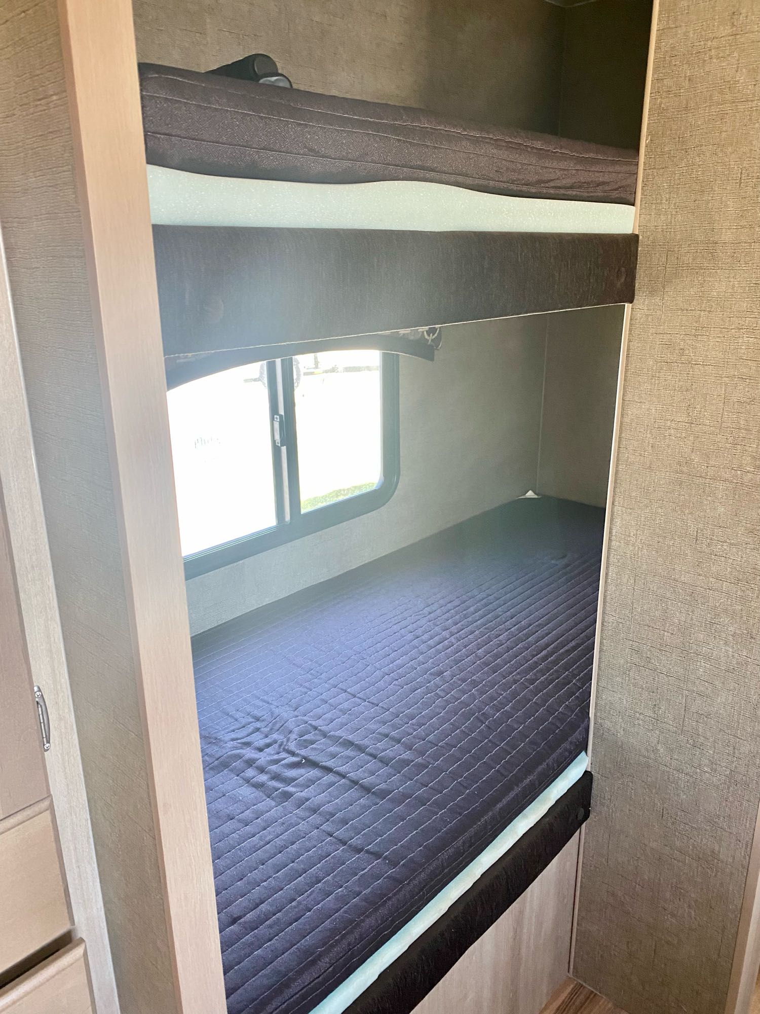 An RV rental's sleeping area with two neatly made bunk beds, dark mattresses, and a window.. Pacific Coachworks Other 2016