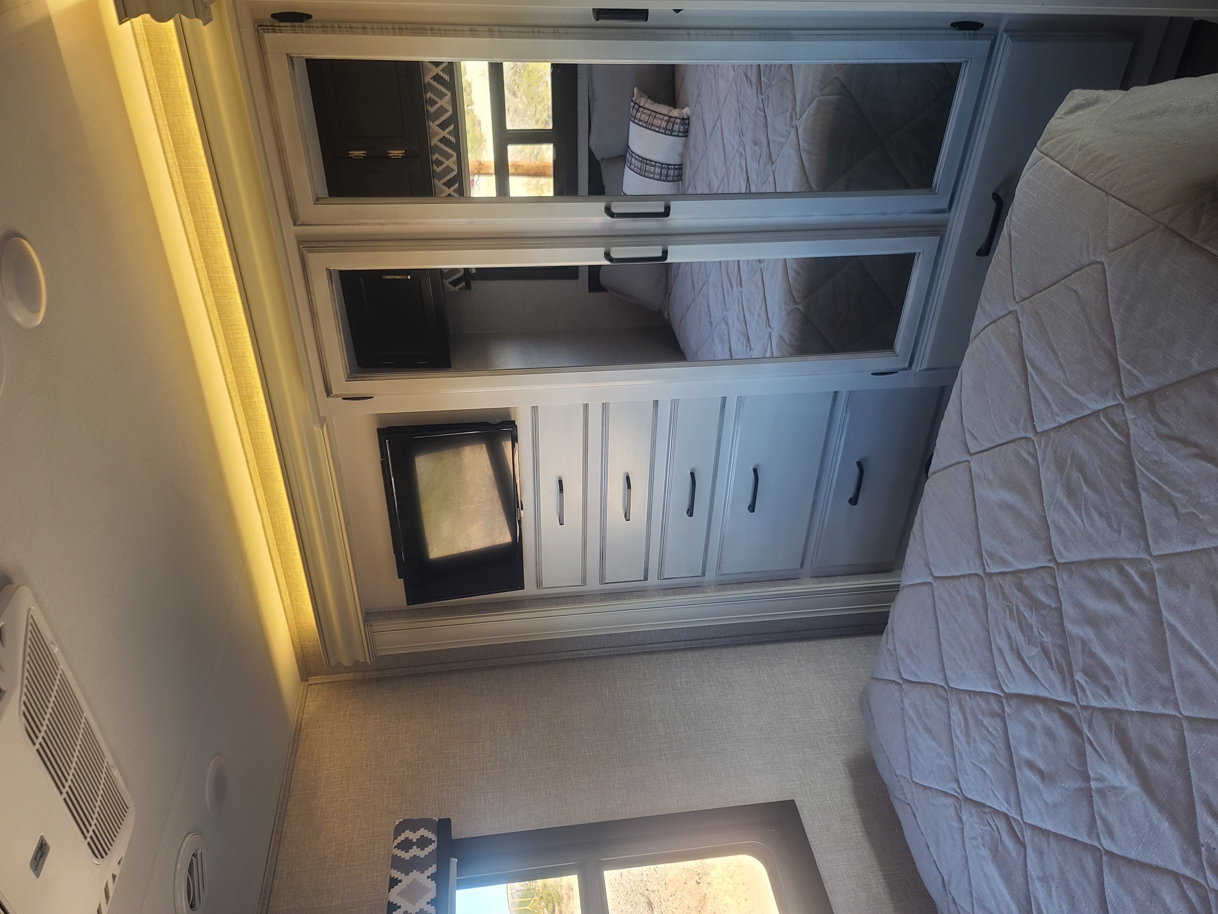Inside an RV rental: a compact bedroom features a bed, mirrored wardrobe, TV, and storage drawers.. Entegra Vision 29F 2022
