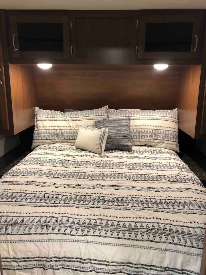 Inside an RV rental: a cozy bedroom with patterned bedding, overhead cabinets, and soft lighting.. Jayco Jay Flight 2018