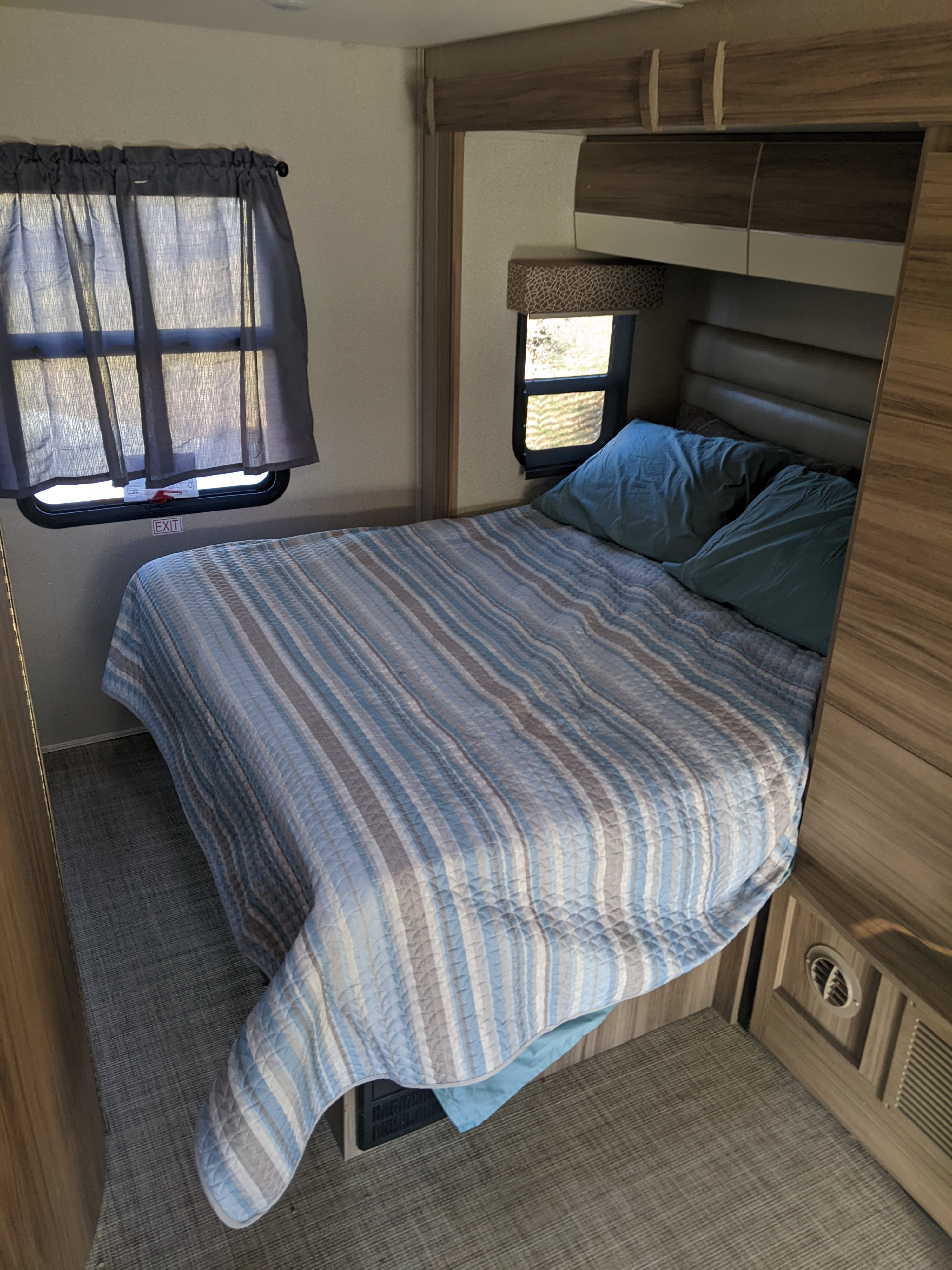 This RV rental bedroom offers a quilted bed with blue and grey stripes, windows, and integrated cabinetry. Compact & inviting.. Jayco Melbourne 2018