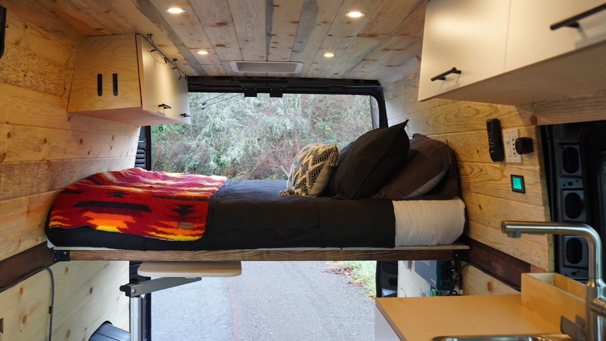 Cozy rv rental interior: wood-paneled walls, comfortable bed, kitchen. Ideal for van life & travel adventures.. Dodge Ram Promaster 2500 2021
