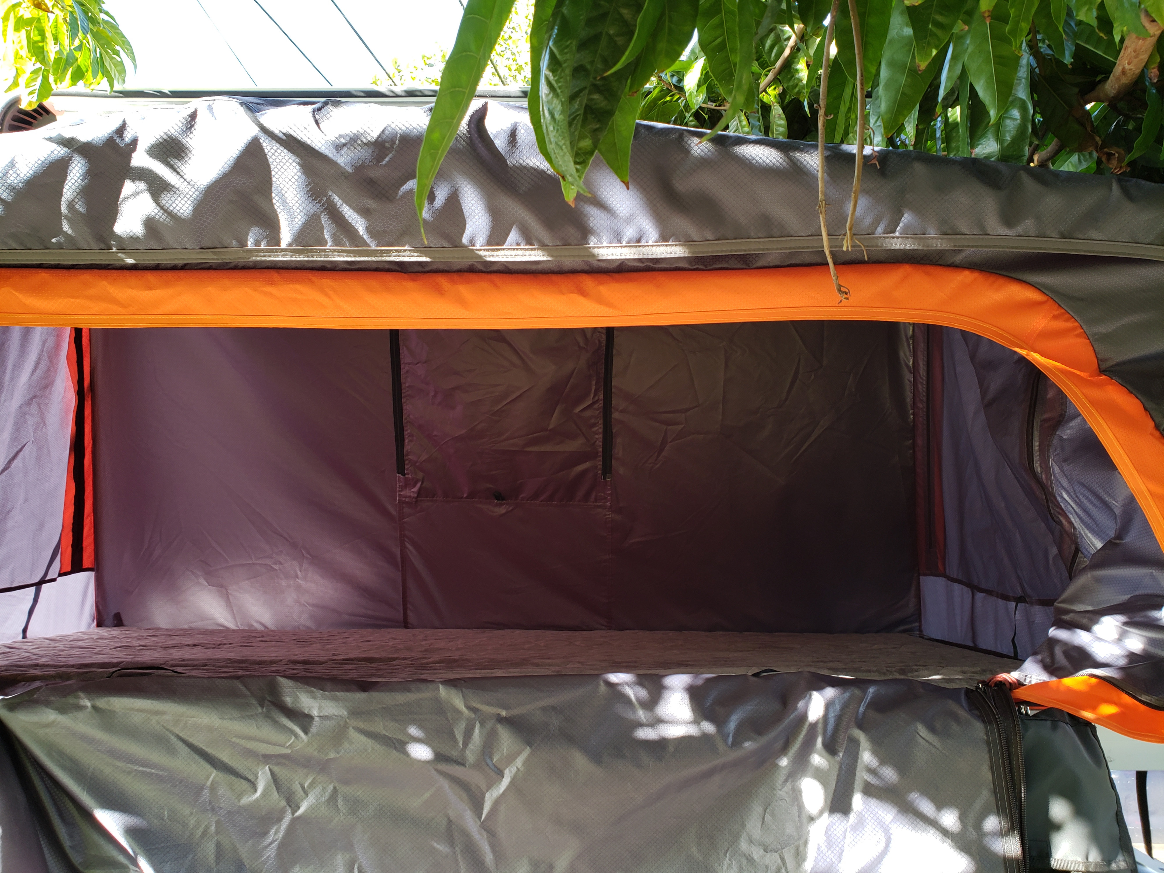Inside a comfortable RV rental rooftop tent, featuring grey fabric walls, orange accents, and a sleeping platform.. NISSAN XTERRA 2014