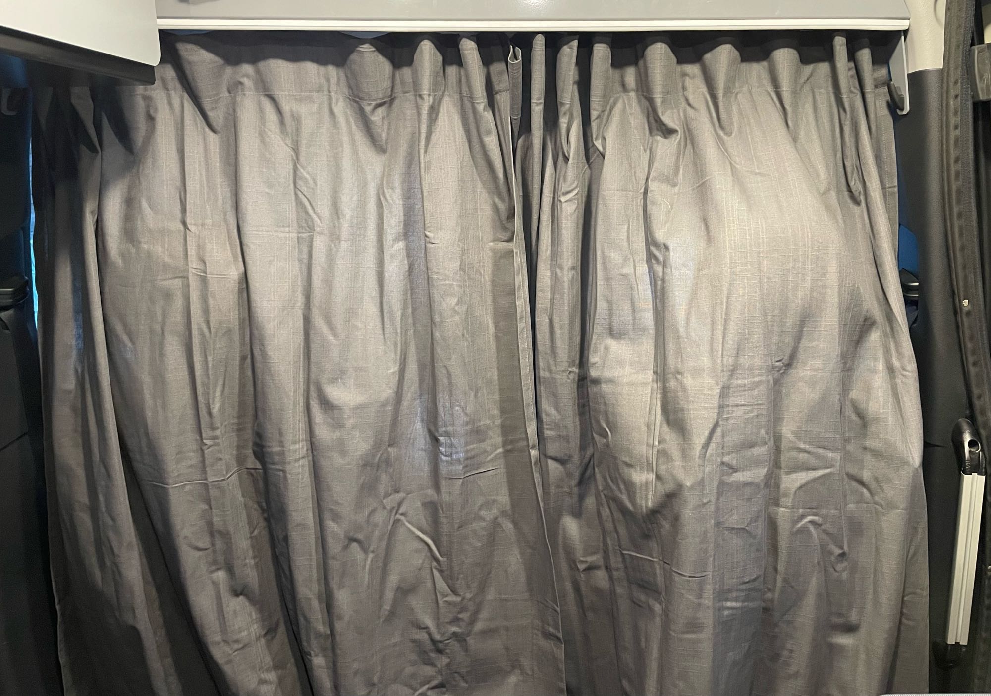 Dark grey textured privacy curtains, hung from a track in an RV rental, effectively blocking light.. Winnebago Revel 2022