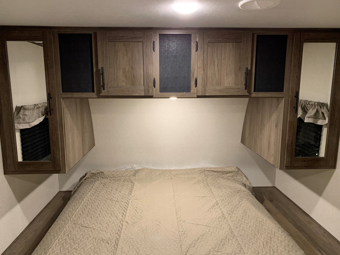 Clean RV rental bedroom with an inviting bed, sleek wood-look overhead cabinets, and integrated bedside mirrored wardrobes.. Prime Time Avenger 2021