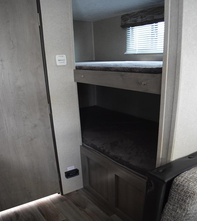 Cozy bunk beds inside an RV rental, featuring a thermostat and window, perfect for family travel adventures.. Forest River X-Lite 2020