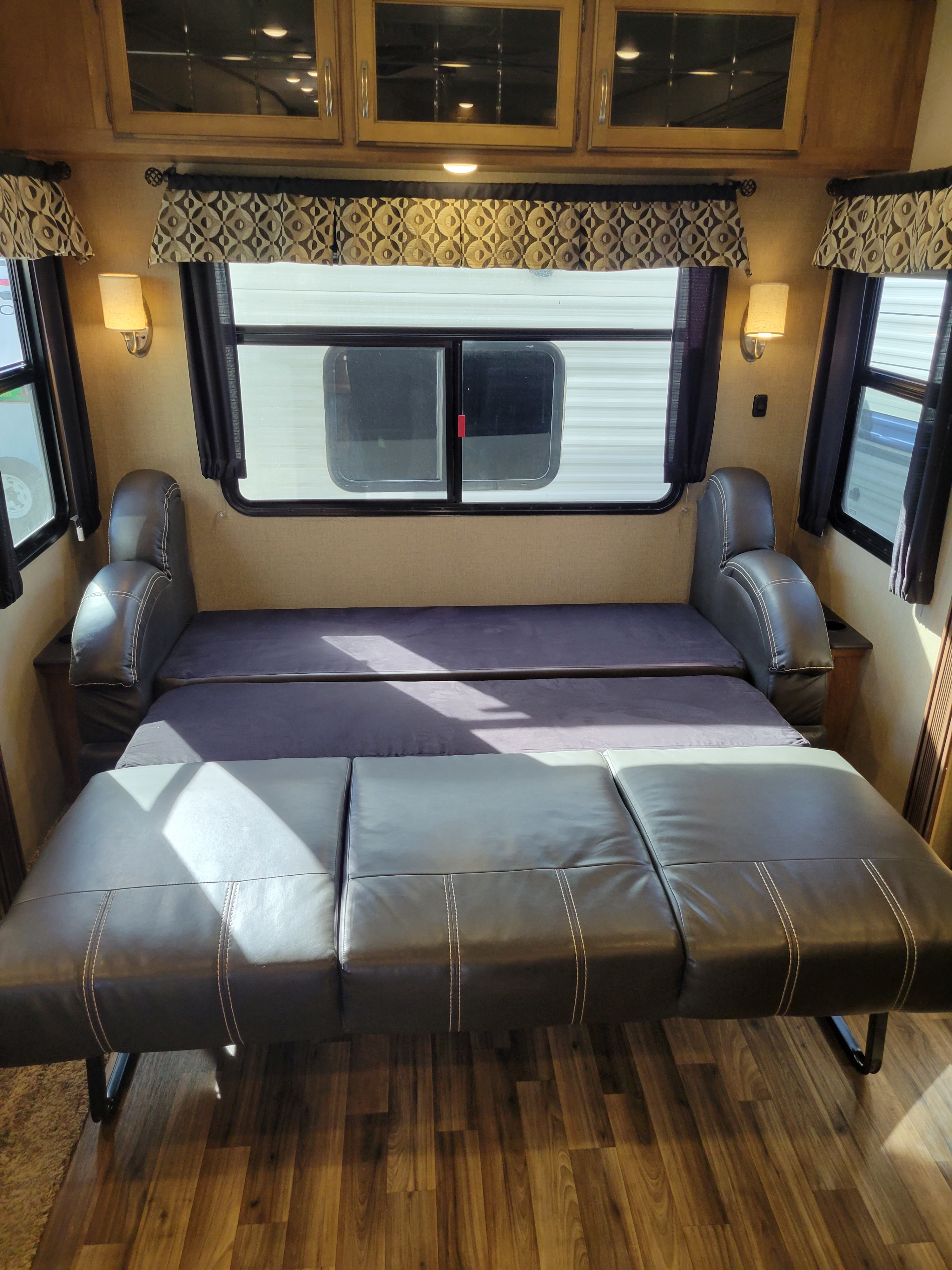 RV rental interior: sofa converted to bed, with windows, overhead cabinets, and wood flooring.. Forest River Chaparral 2017
