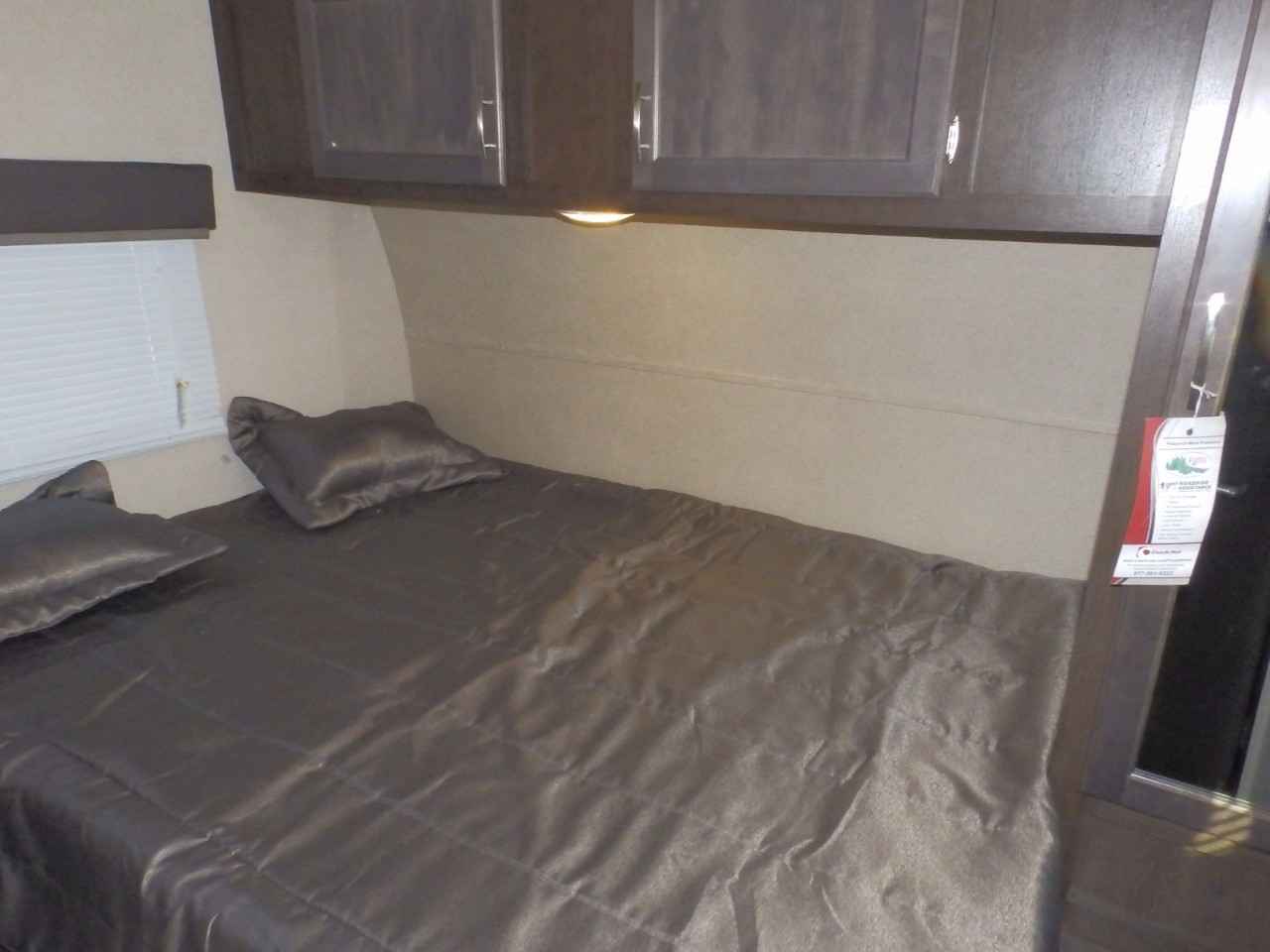 Interior of an RV rental bedroom with a full bed, pillows, overhead storage, and window.. Forest River 211SLC 2018