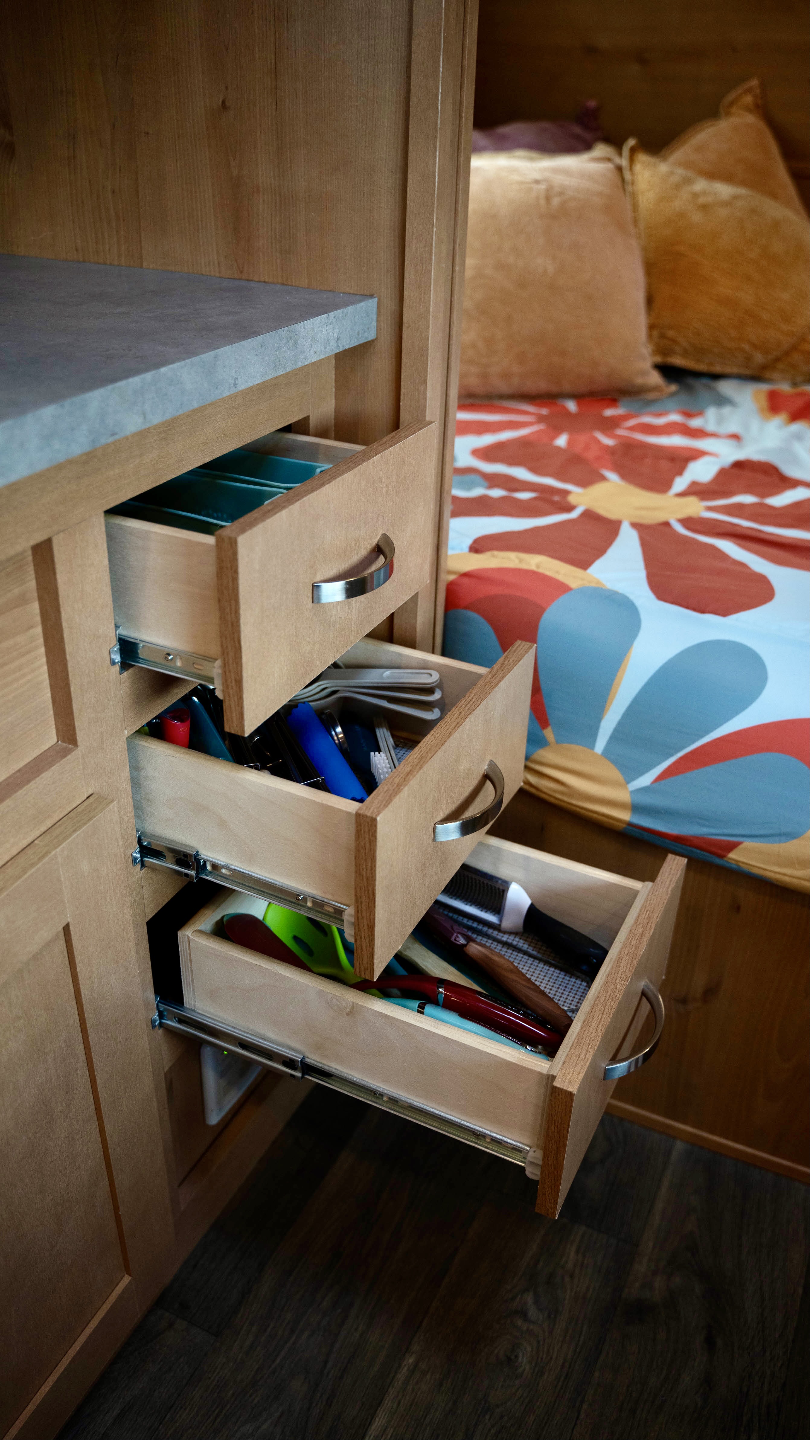 Open kitchen drawers in a clean RV rental, revealing organized utensils & small items. Cozy bed with floral bedding visible.. Old School 818 2021
