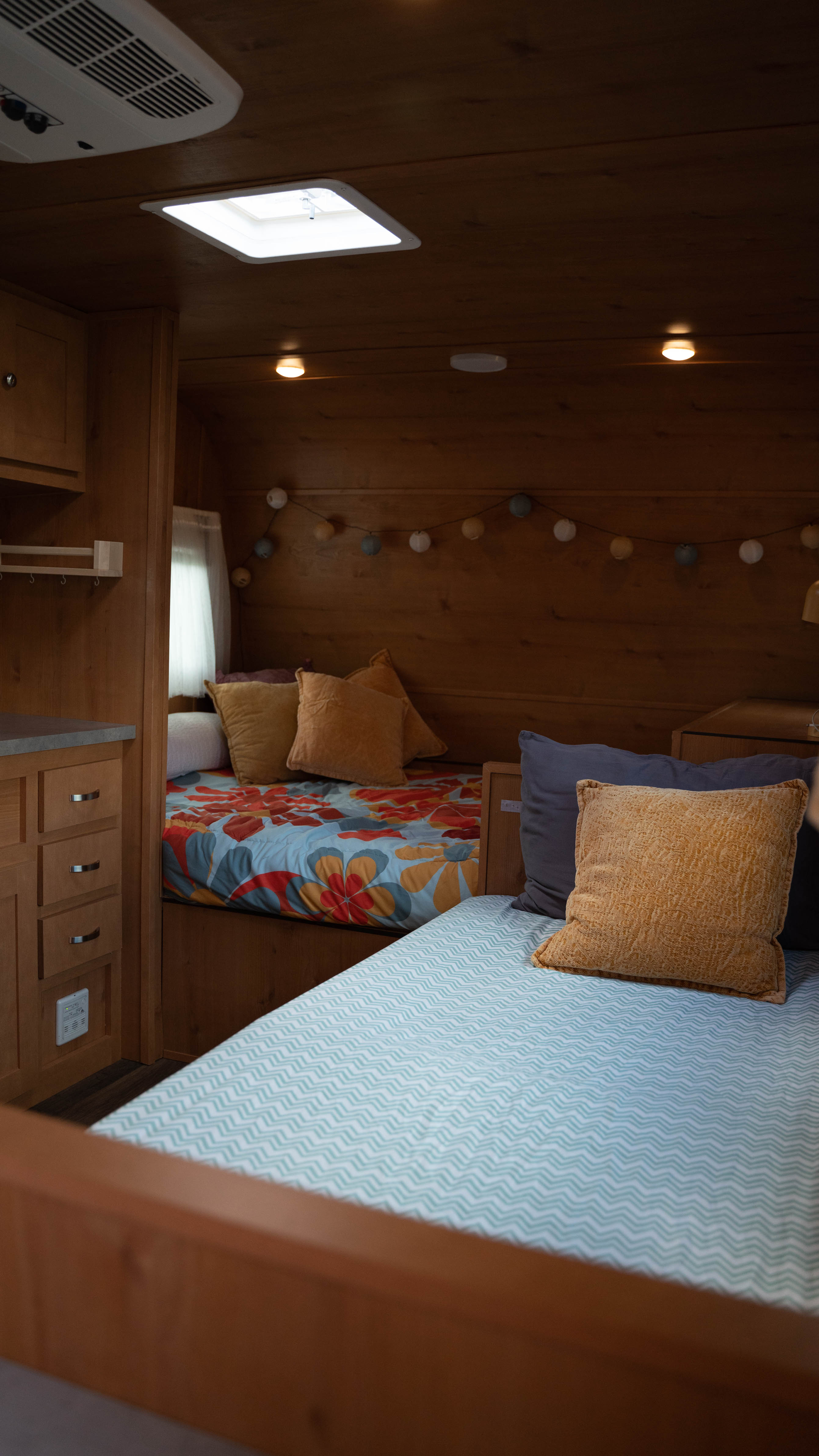 Explore a cozy RV rental interior: two inviting beds with colorful bedding, wood paneling, & ambient string lights.. Old School 818 2021