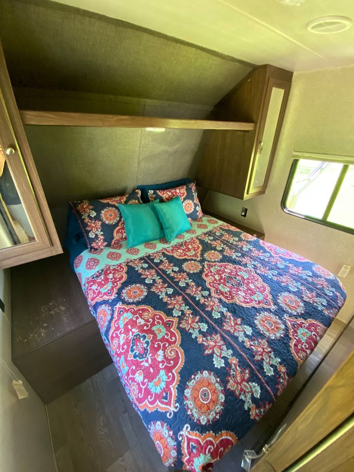 Cozy RV rental bedroom featuring a colorful patterned bedspread, teal pillows, and built-in storage. Ideal for travel.. Heartland Prowler Lynx 2018