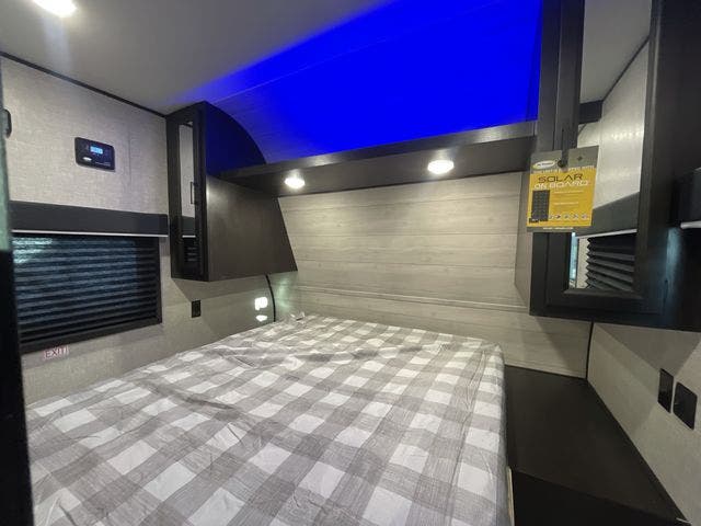Interior view of an RV rental bedroom, showcasing a plaid bed, window with blinds, overhead storage, and solar power tag.. Jayco Jay Flight SLX 2022