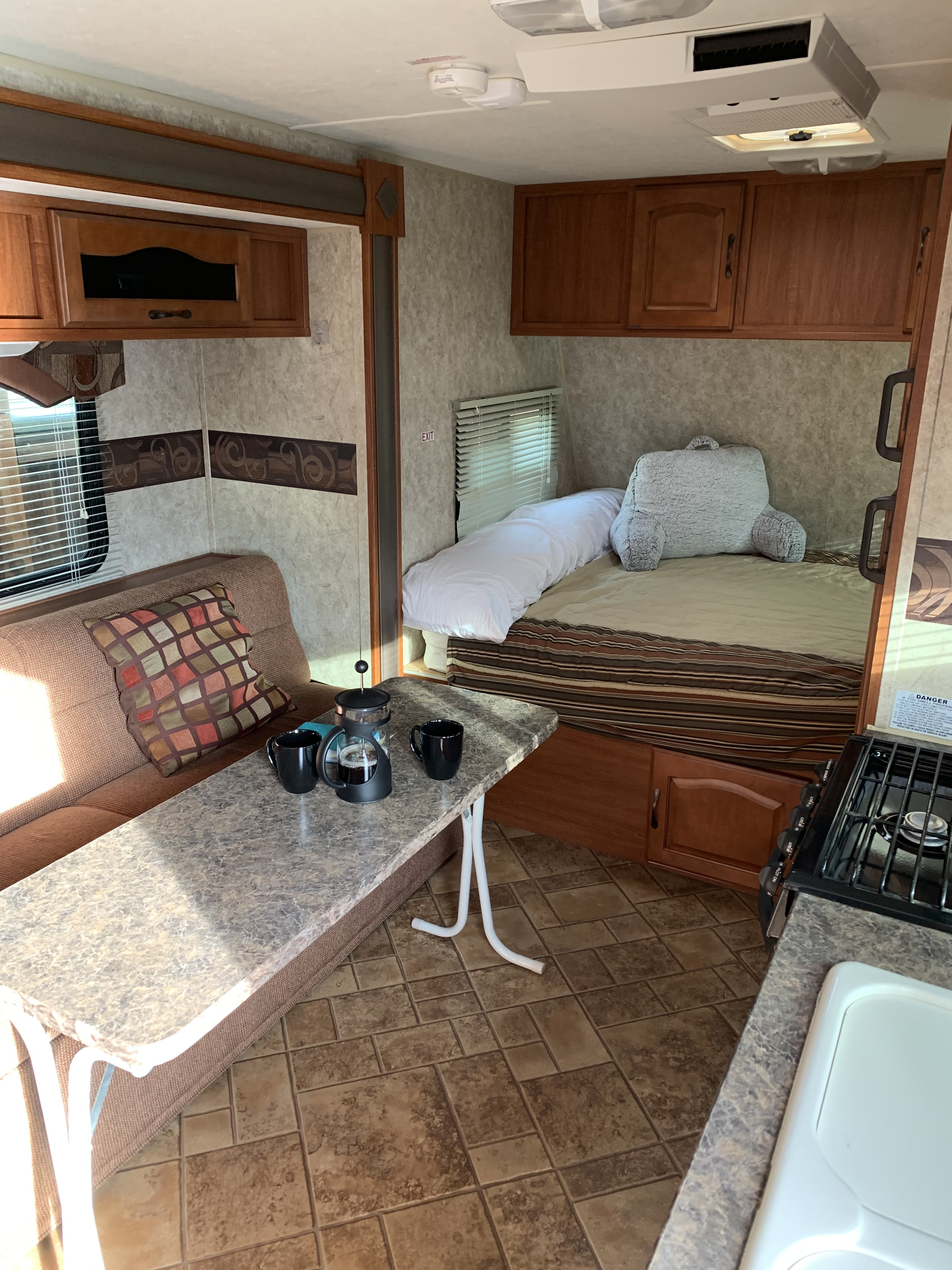 Bright RV rental interior with a cozy bed, coffee setup on a table, and kitchen for your next adventure.. Forest River Surveyor 2015
