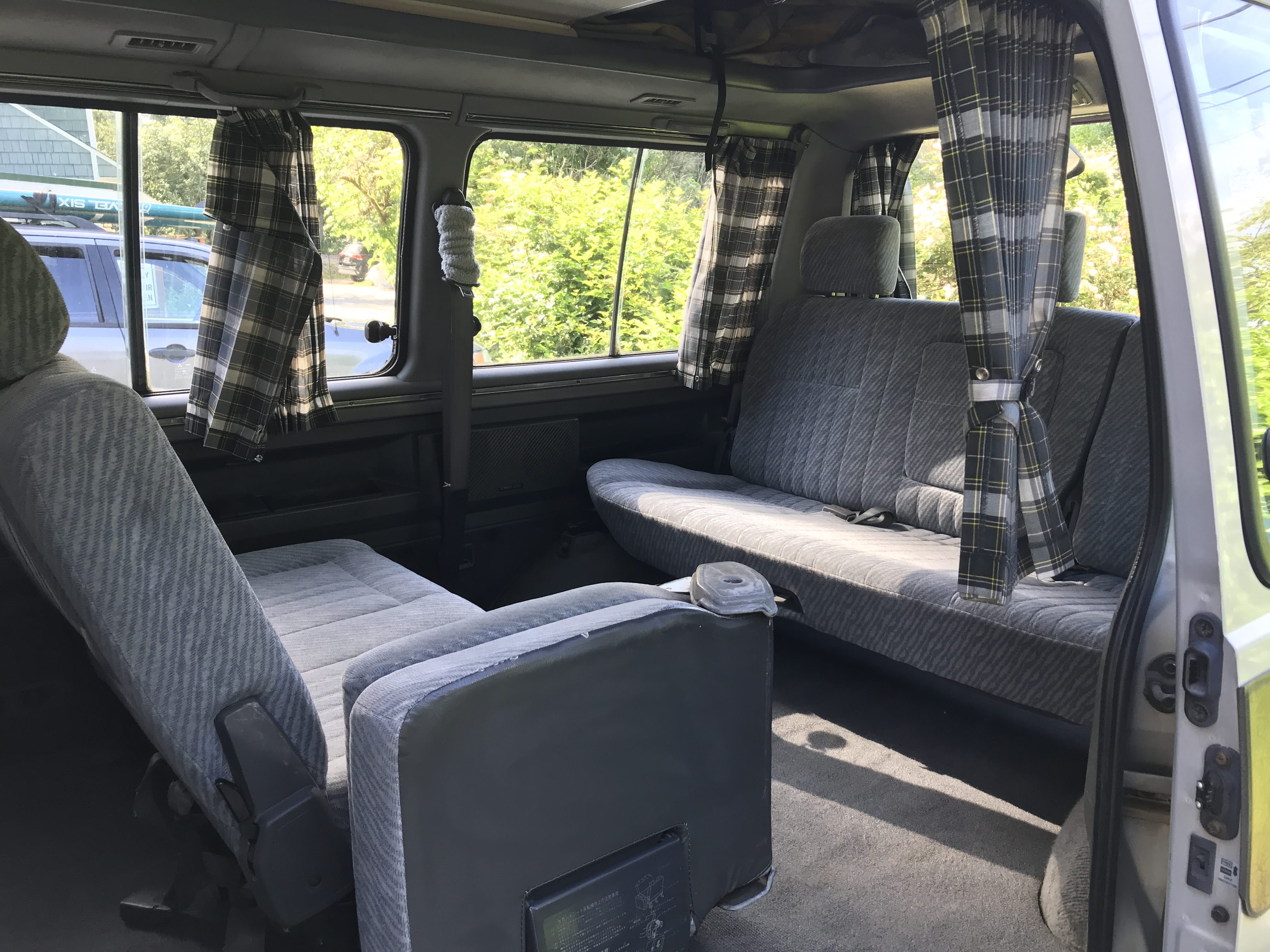Spacious RV rental interior with comfortable grey seating and plaid window curtains, ready for your next adventure.. Mitsubishi Delica 1994