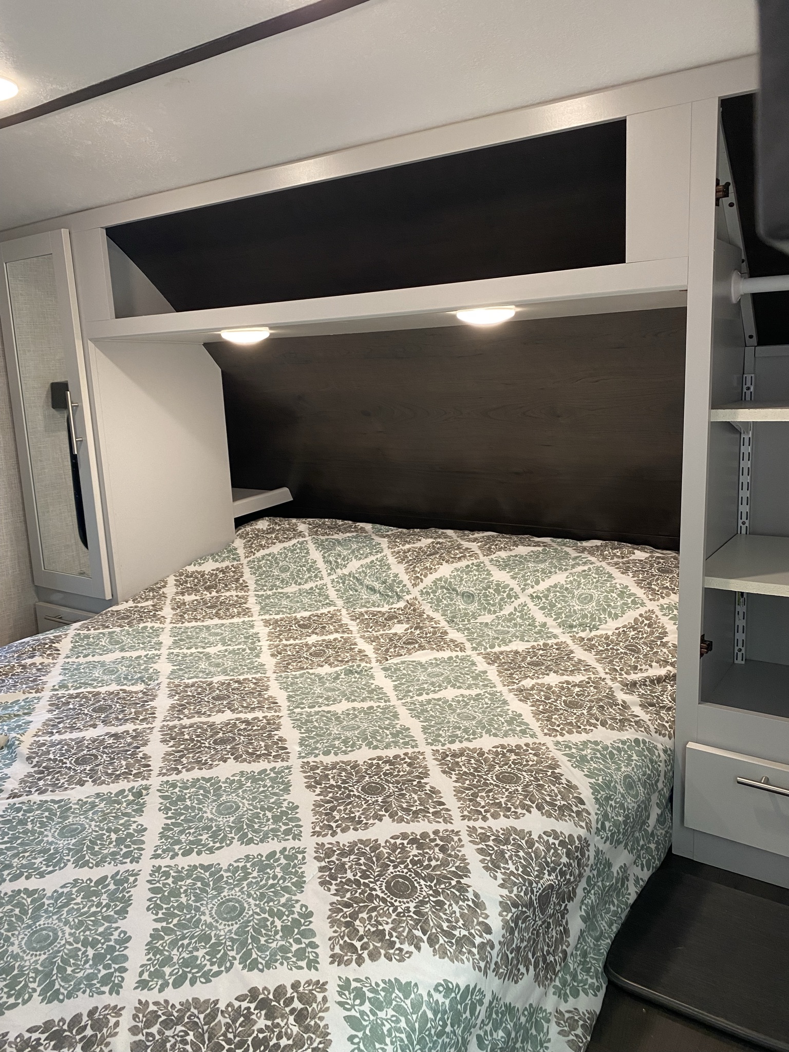 RV rental bedroom showcasing a patterned bed, overhead lighting, and built-in storage. A compact and functional camper interior.. Keystone RV Bullet Ultra Lite 2020