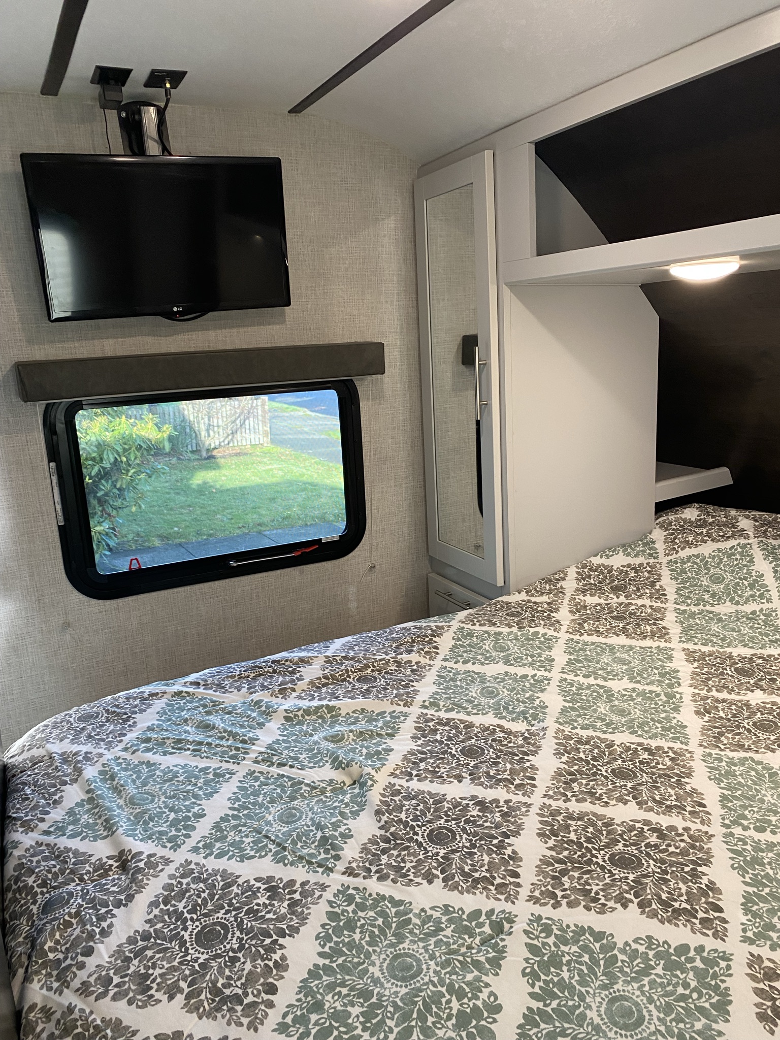 Cozy RV rental bedroom with patterned bed, wall-mounted TV, window, and built-in storage.. Keystone RV Bullet Ultra Lite 2020