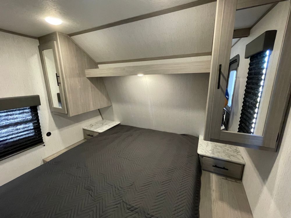 Inside this RV rental, a comfy bedroom features a large bed, overhead storage cabinets, nightstands, and window blinds.. Coleman Lantern 300tq 2022