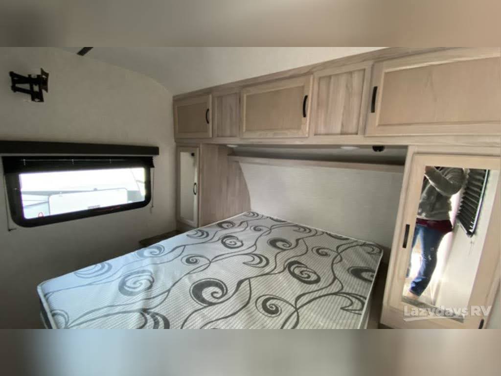 Step into a comfortable RV rental bedroom featuring a patterned bed, overhead storage, window, and large mirror, perfect for your travel adventures.. Coachmen 3379 BH 2020