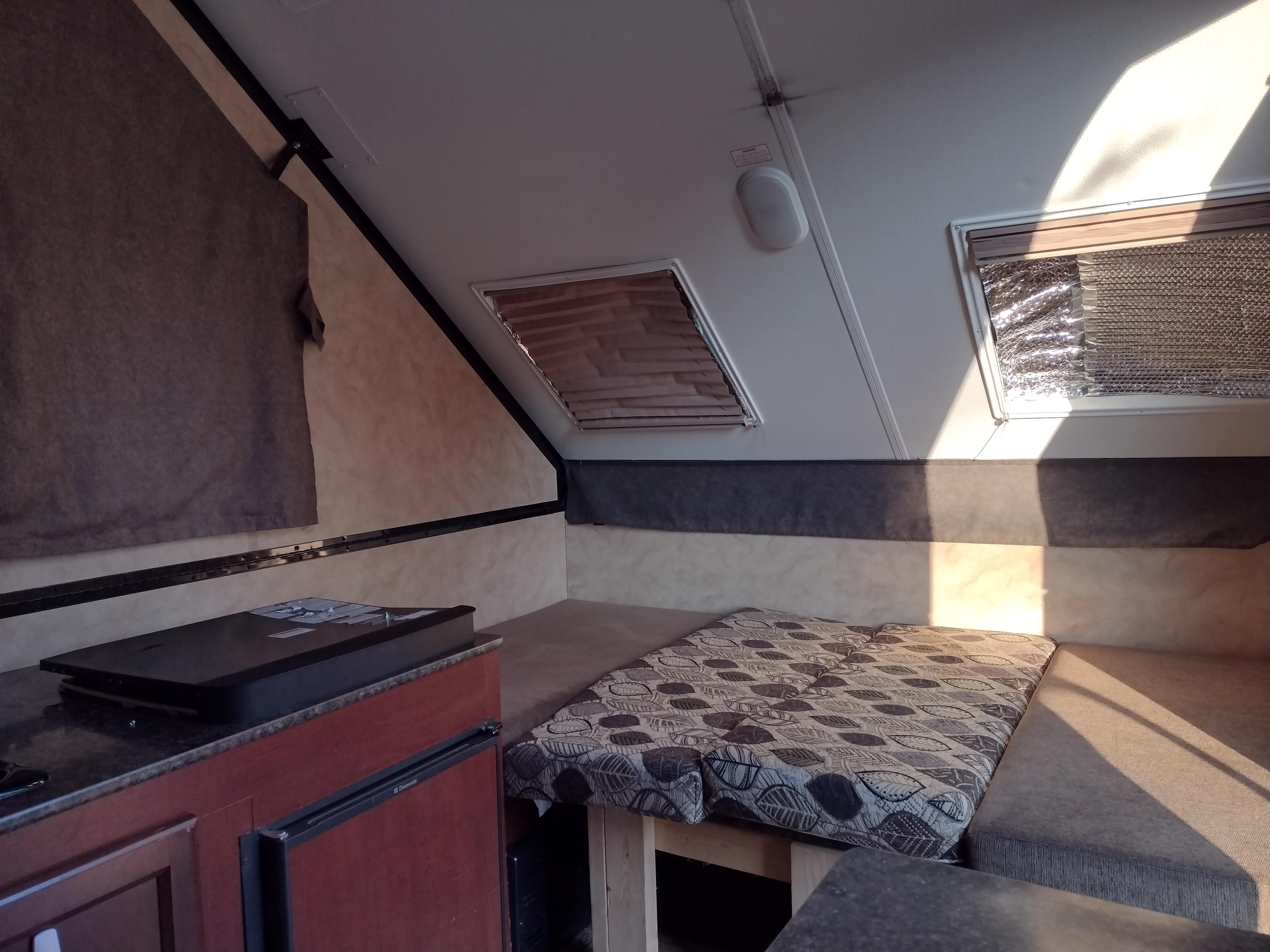 Inside a bright RV rental: features a cozy bed with patterned cushions, a compact kitchen counter, and sunlit windows with shades.. Coachmen Clipper 2016