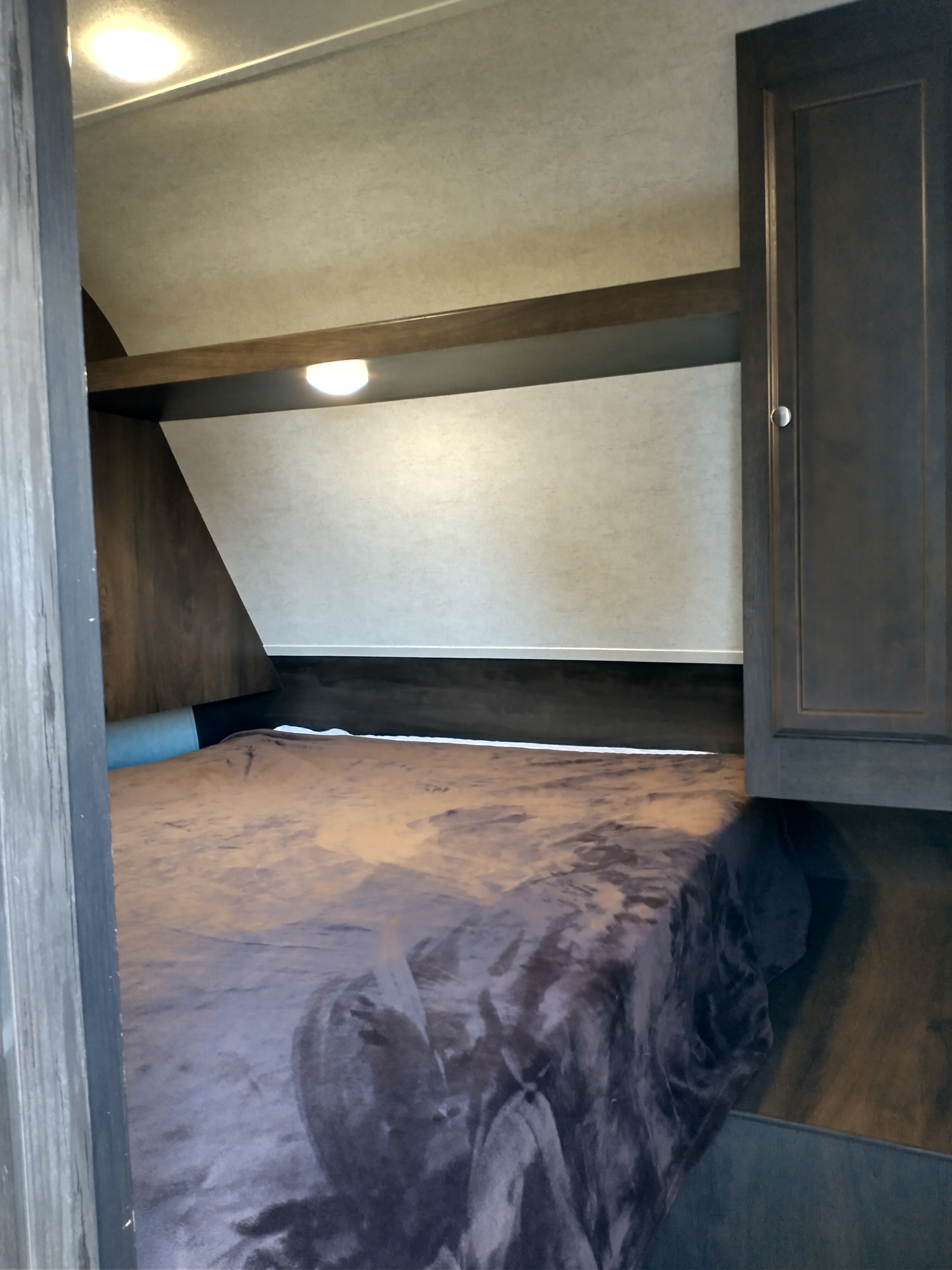 Cozy RV rental bedroom with dark bedding, overhead shelf, and storage cabinets.. Starcraft Autumn Ridge 2019