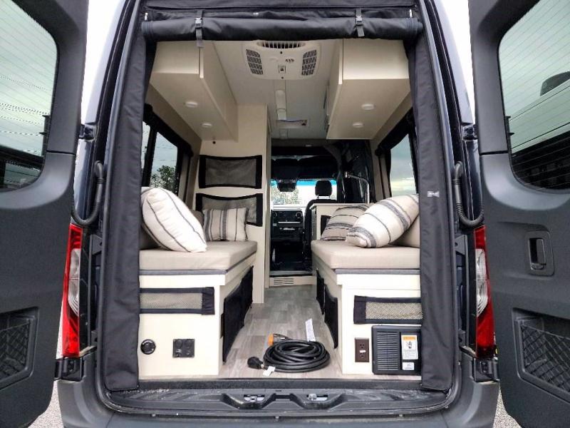 Cozy RV rental interior from the back, showing two cushioned benches, overhead storage, and a power cable.. Tiffin Motorhomes Cahaba 2022